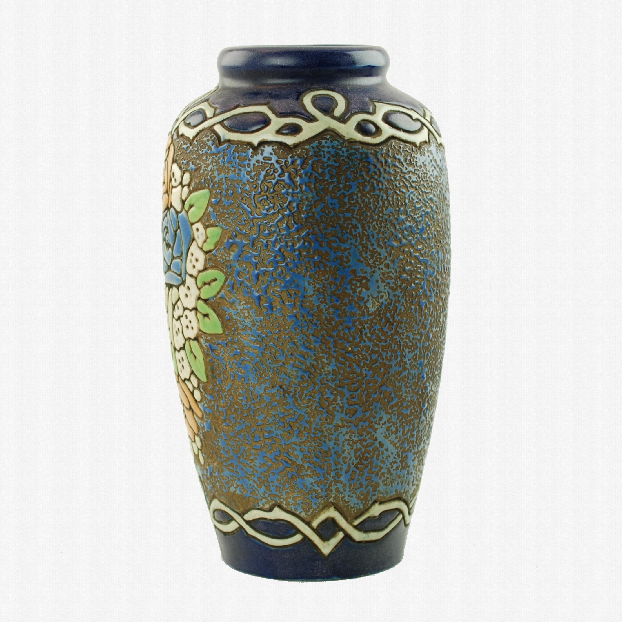 This striking enameled pottery vase was made by Amphora and is decorated with stylized floral decoration set against a textured ground made up of variegated blue enamel paint on a metallic copper field. The floral grouping on the front of the piece