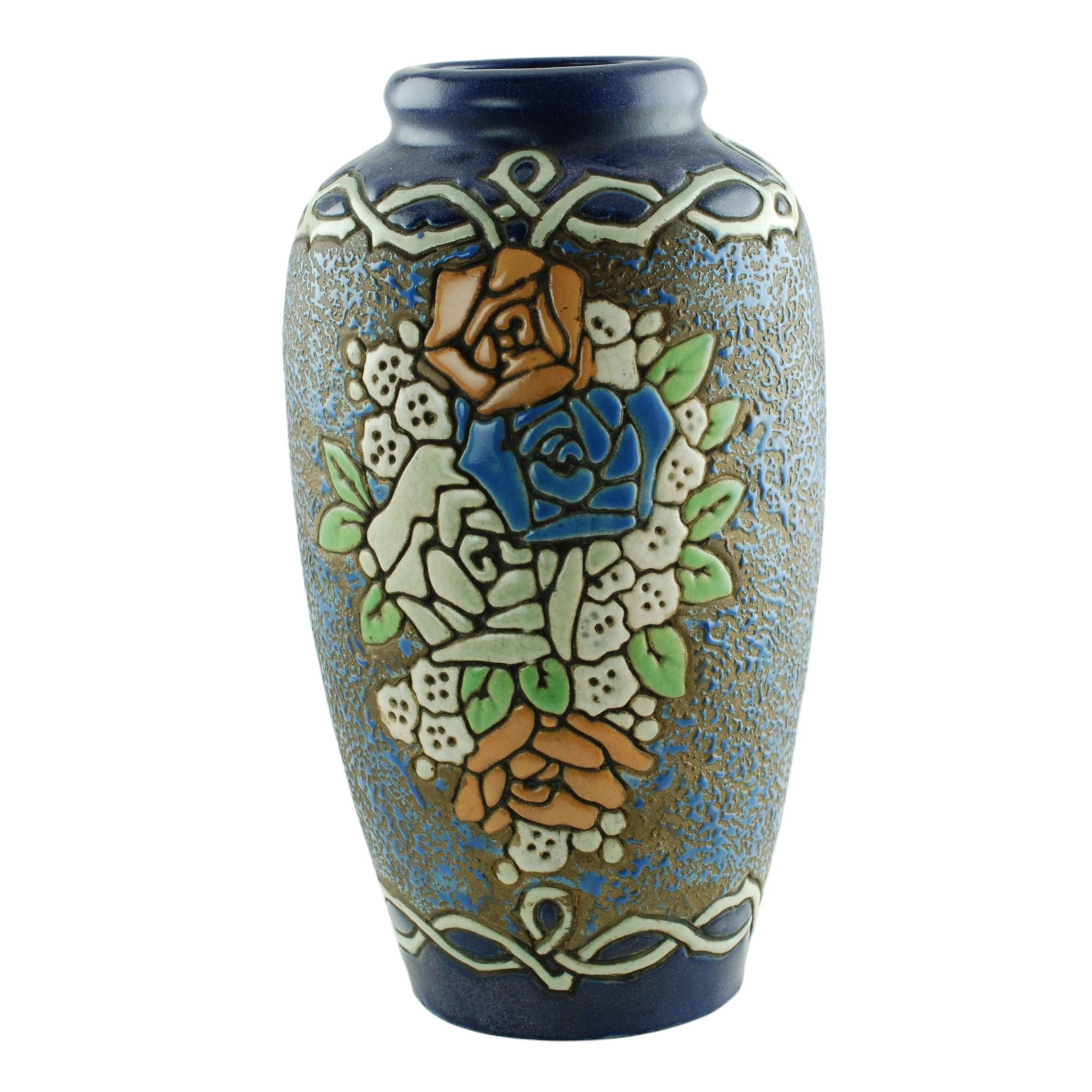 This striking enameled pottery vase was made by Amphora and is decorated with stylized floral decoration set against a textured ground made up of variegated blue enamel paint on a metallic copper field. The floral grouping on the front of the piece