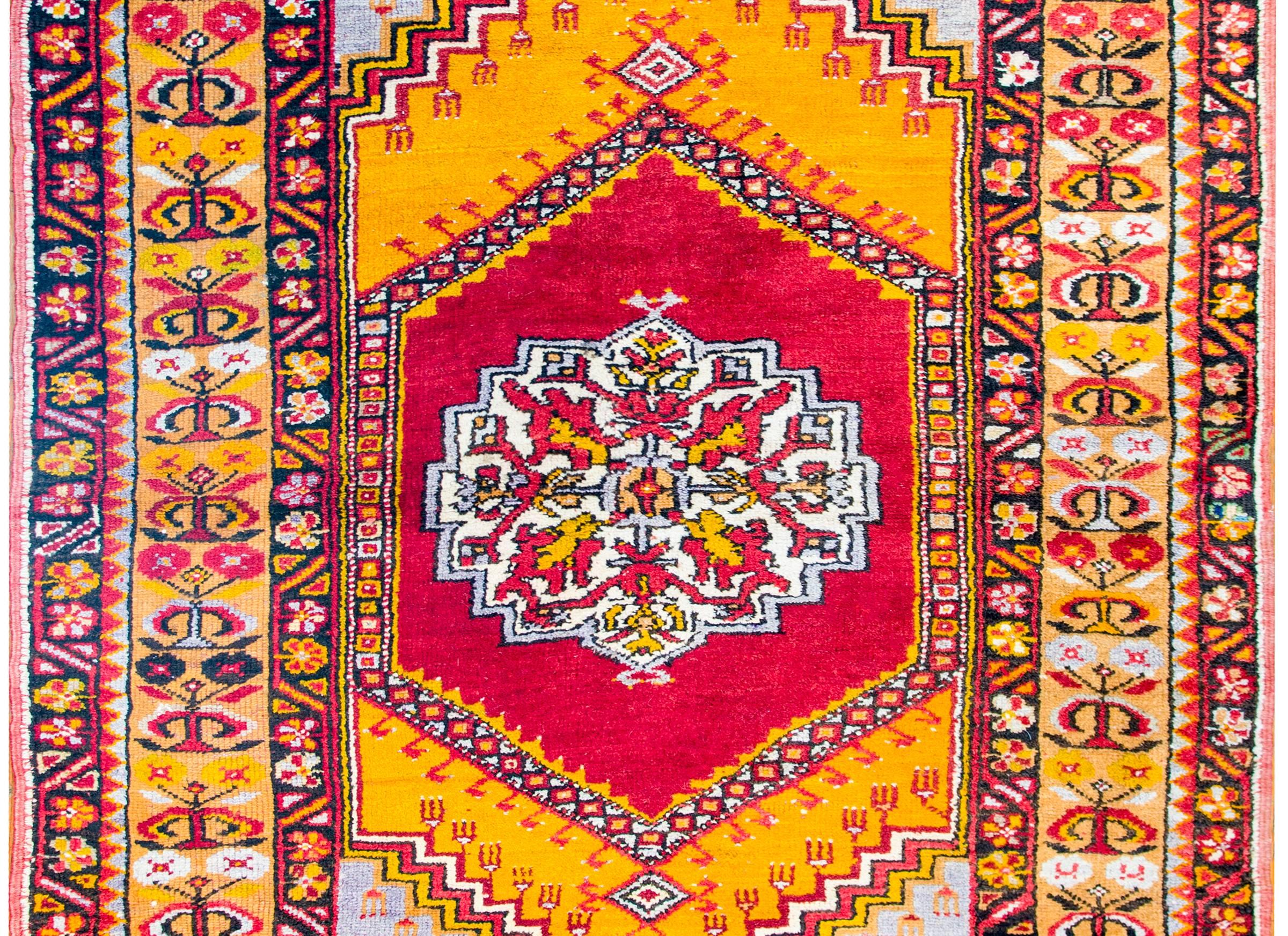 An early 20th century Anatolian Turkish multicolored rug with multiple a large central floral medallion on crimson and gold backgrounds surrounded by a wide floral patterned stripe border, flanked by matching petite floral patterned stripes.