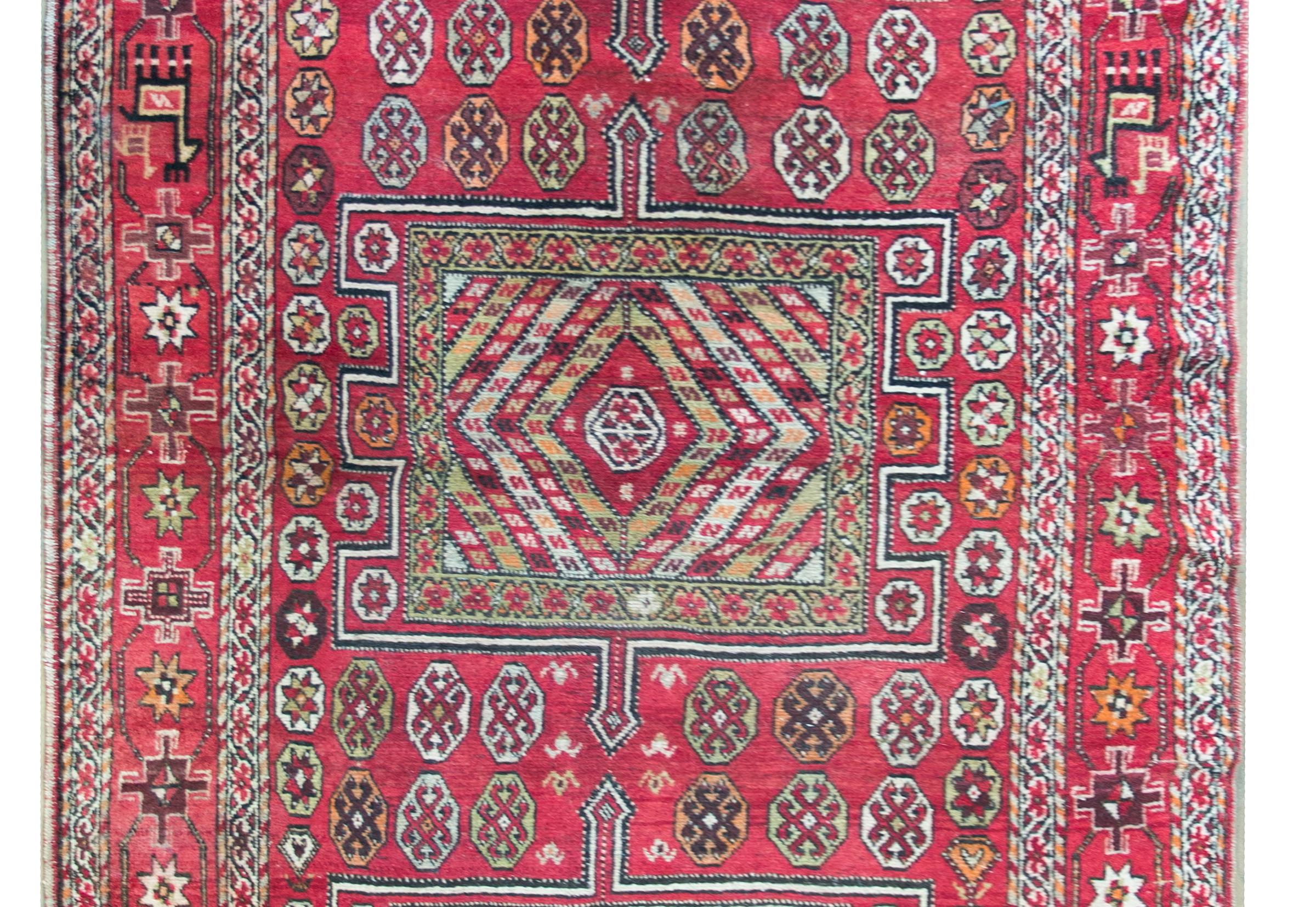 A playful early 20th century Anatolian Turkish rug with three large geometric medallion living amidst a field of stylized flowers, surrounded by several thin floral patterned stripes, and all woven in brilliant crimsons, oranges, pale indigos,