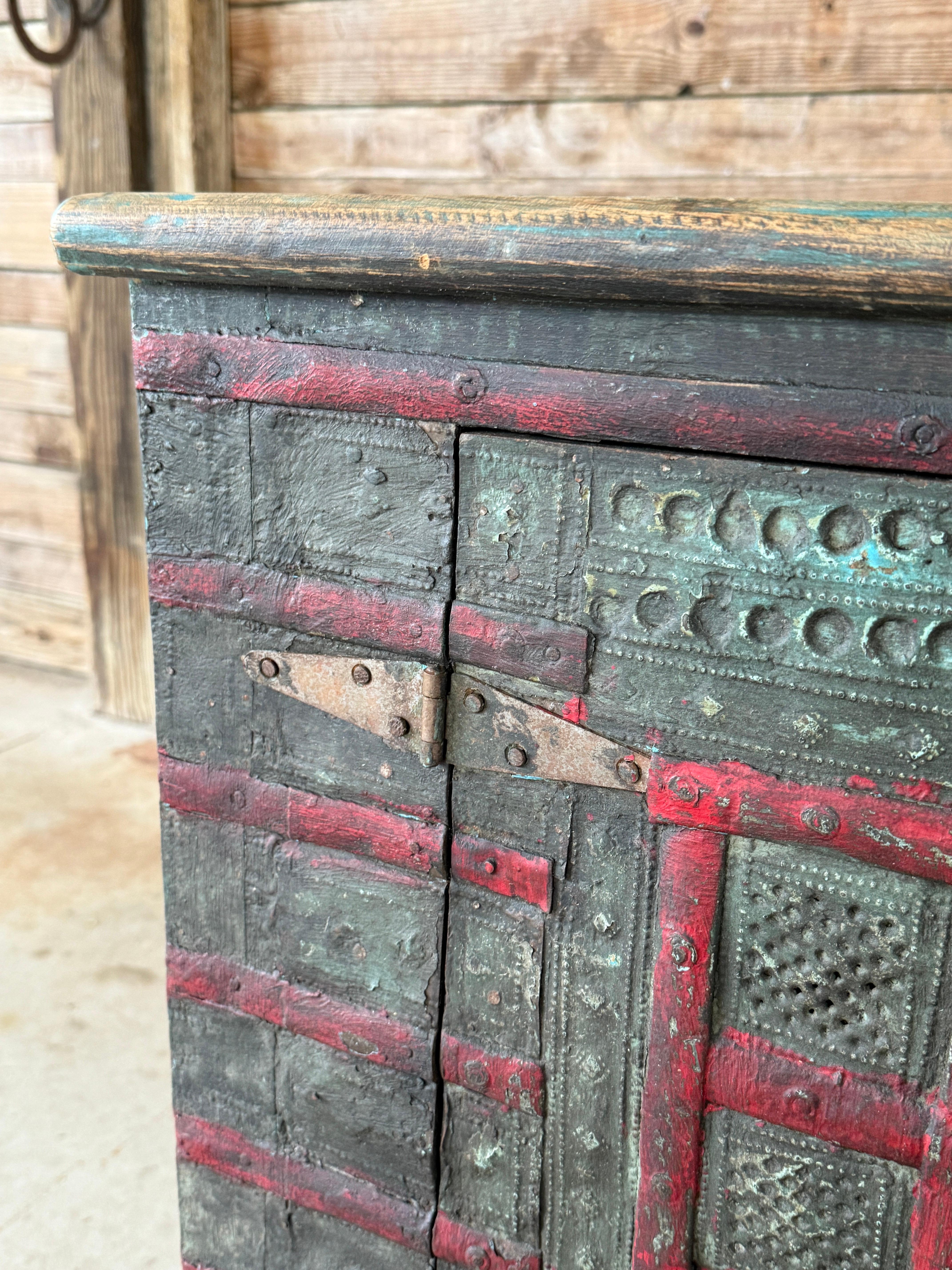 Ein auffälliger antiker anglo-indischer Schrank, reich verwittert mit seiner originalen mehrschichtigen Lackierung in roten und grünen Farbtönen über Naturholz. Aus Massivholz gefertigt und mit handgestanzten Holzpaneelen und eisernen