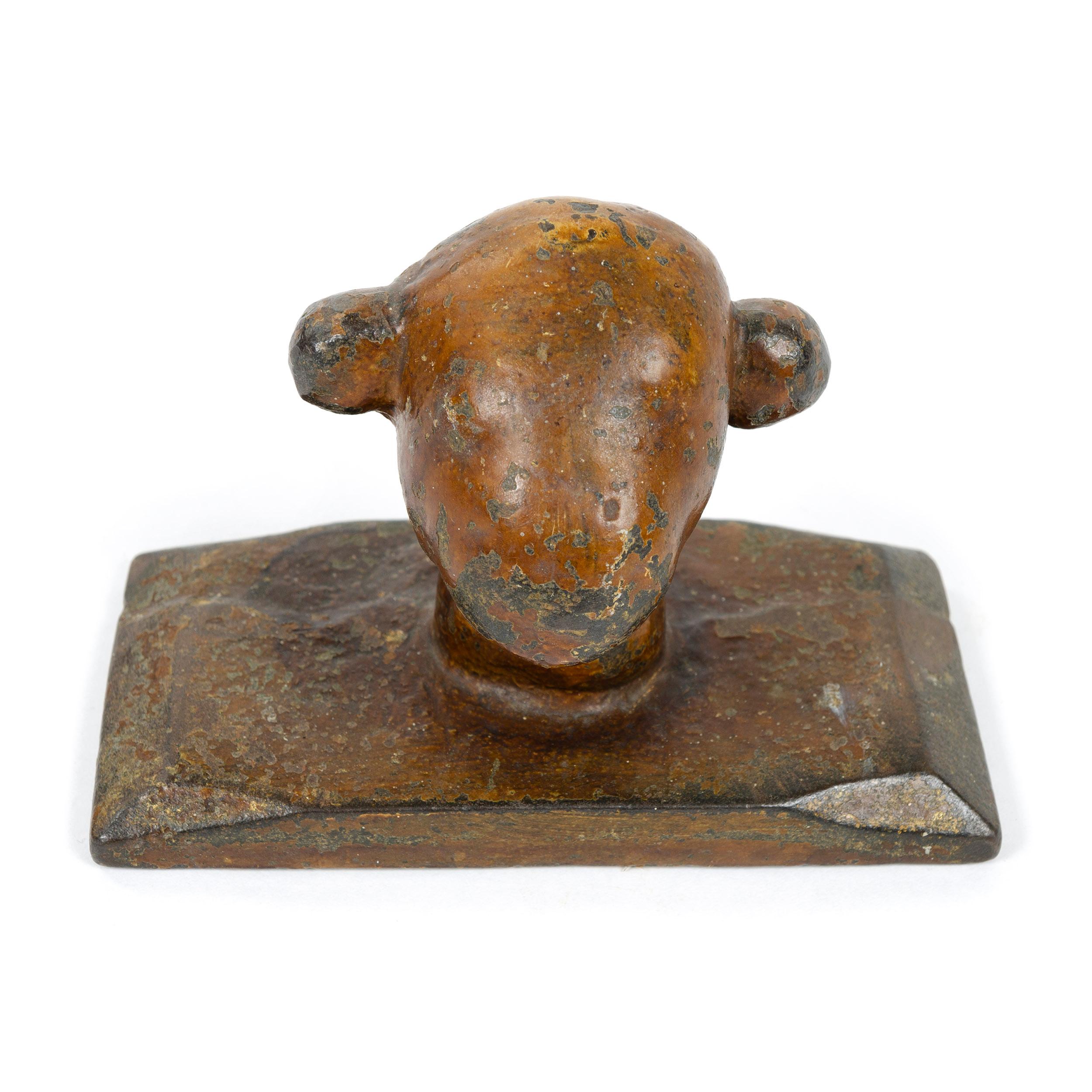 An antique, whimsical iron paperweight of substantial size and heft with a natural, medium to darker brown patina which shows appropriate signs of warmth and age. Best described as a stylized animal head, likely a lamb, joined to a rectangular iron