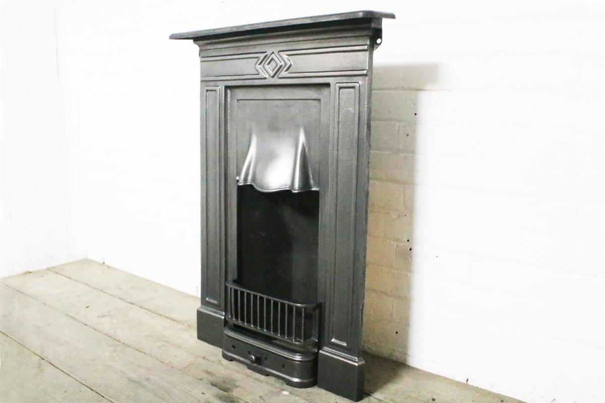 Early 20th century antique cast iron bedroom fireplace, circa 1910. 

Measures: Shelf 71 cm wide x 11.5 cm deep. Overall 97 cm high. Footprint 63 cm wide. 

Finished with traditional black grate polish and complete with a new clay fire back and