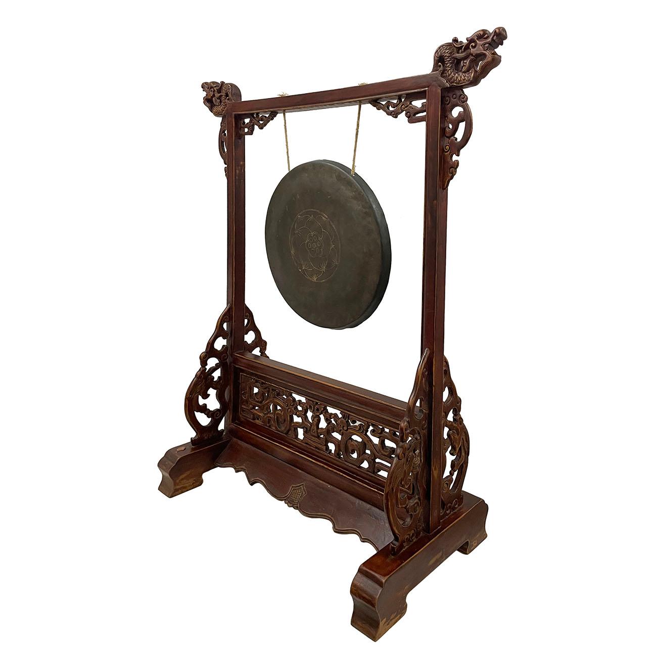 This antique Chinese table gong is hanging on a carved wood stand. It features beautiful carved fretwork on the bottom and detailed carving work of decorated dragons on the top of the wood frame. This antique gong is 100% hand made with the lotus