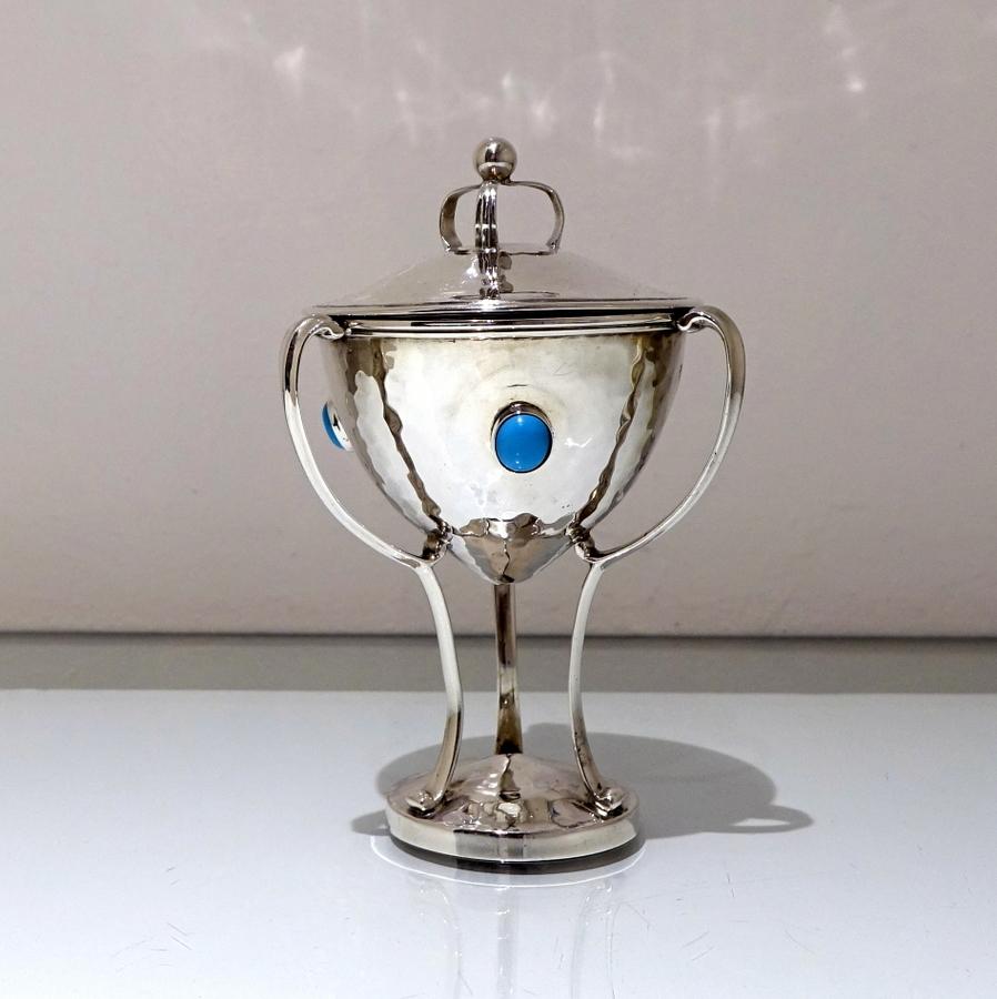 A highly desirable hammered finished miniature three handled cup and cover stylishly decorated with inset semi-precious stones around the centre of the bowl.

 

Measures: Weight 9.8 troy ounces/306 grams

Height: 6.5