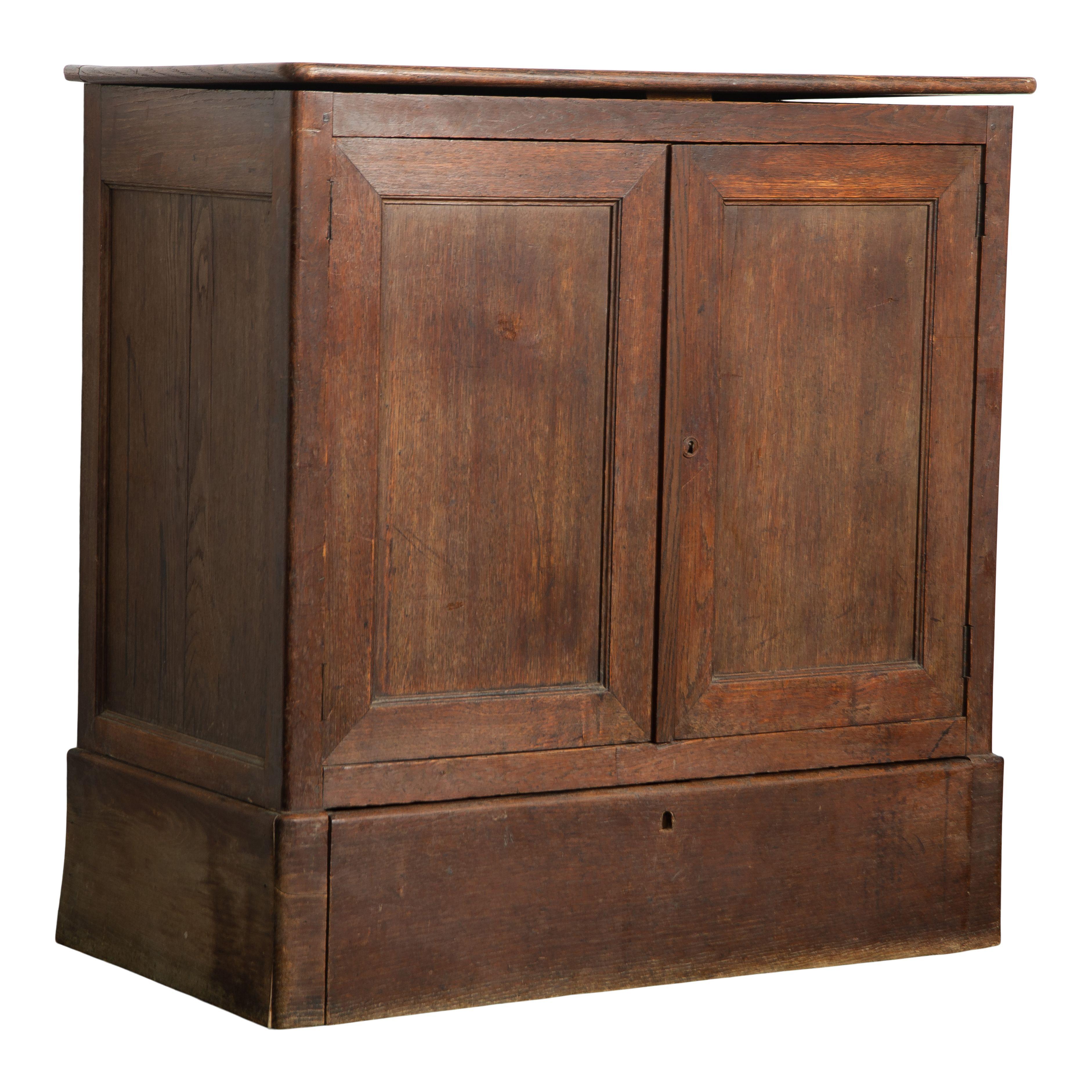 A vintage French wood cabinet with shelves. This cabinet features a simple and classic design with two cabinet doors. The doors open to two shelves, and the top opens upwards, providing plenty of storage space. The wood has a dark stain and there is
