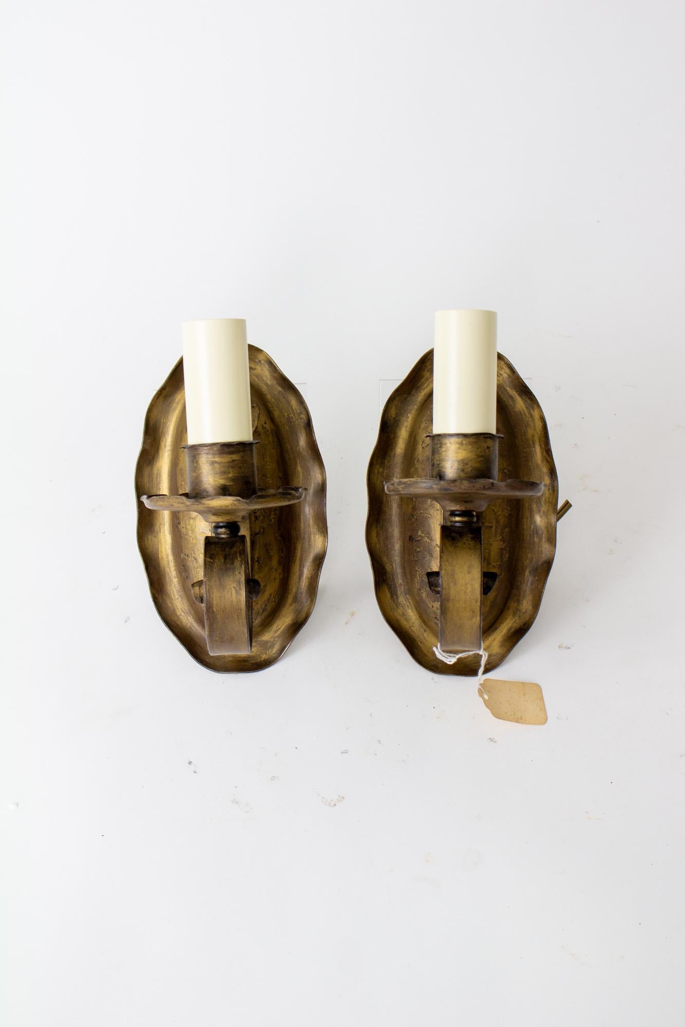 Early 20th century antique gold oval sconces, a pair. Metal sconces with the original black with antiqued gold wash finish. Single curved arm, Oval backplate with a ruffled edge. Rewired with new candlecovers, complete and ready for installation.