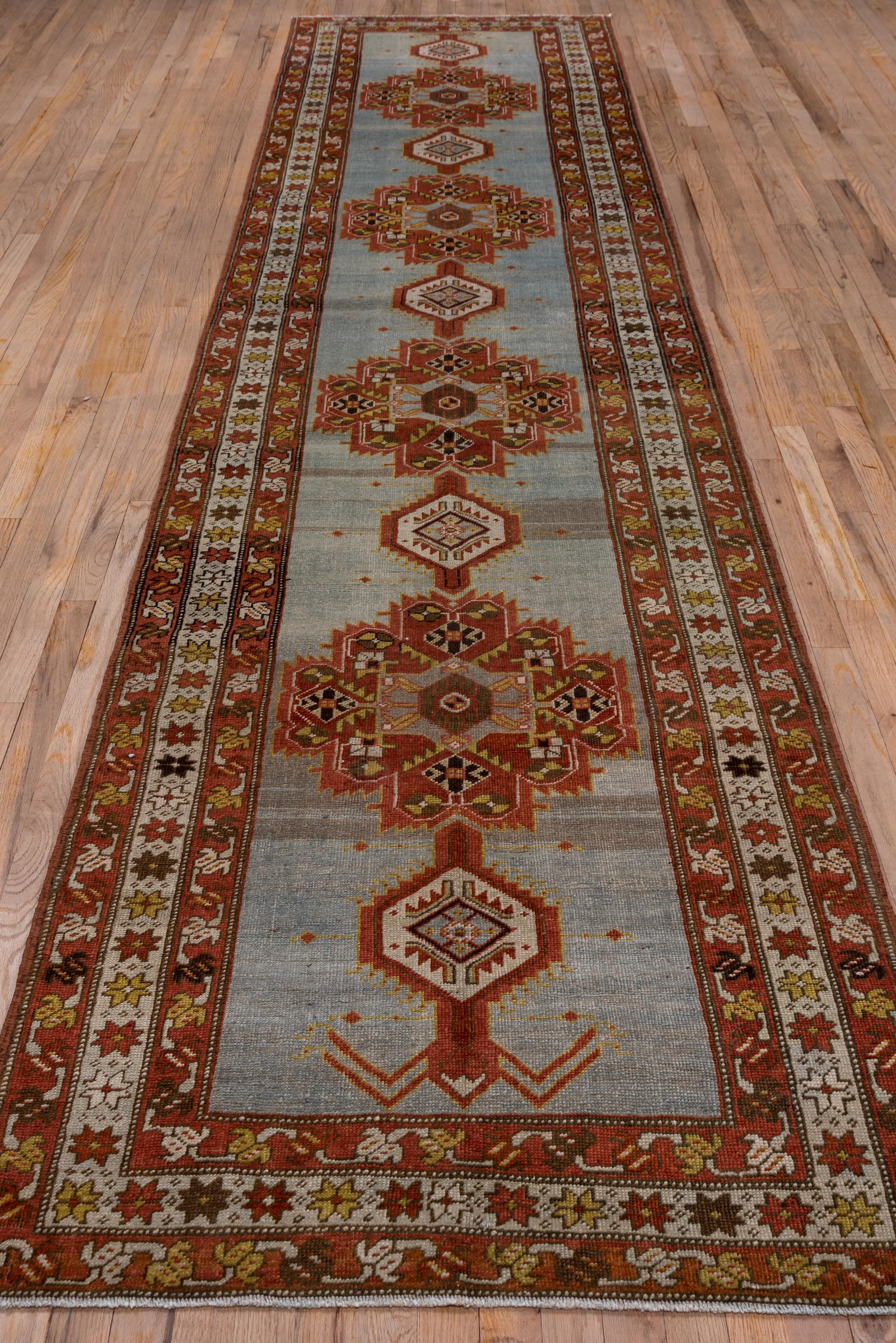 The well-abrashed green field displays four 12-lobed red-brown medallions interspersed with smaller stepped ivory hexagons. The medallions are in the Afshar tribal style. A central ivory star border is flanked by red-brown minors with flip-flop vine