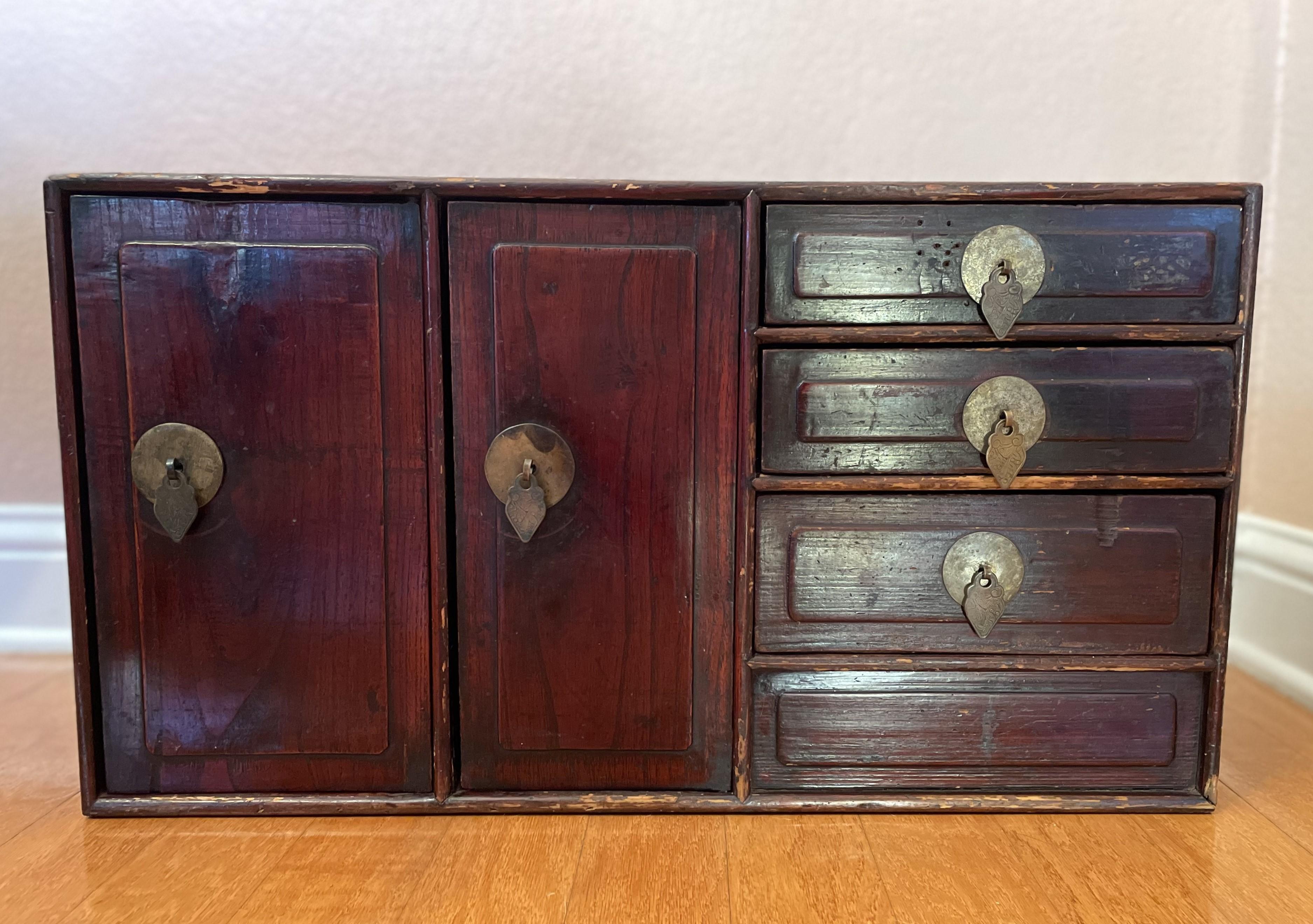 An antique Japanese Tansu with soulful Wabi-Sabi. It appears to be made of Elmwood with finely engraved brass hardware that has a subtle green patina, with an overall soft luster to the wood. This piece fits beautifully atop a console behind a study