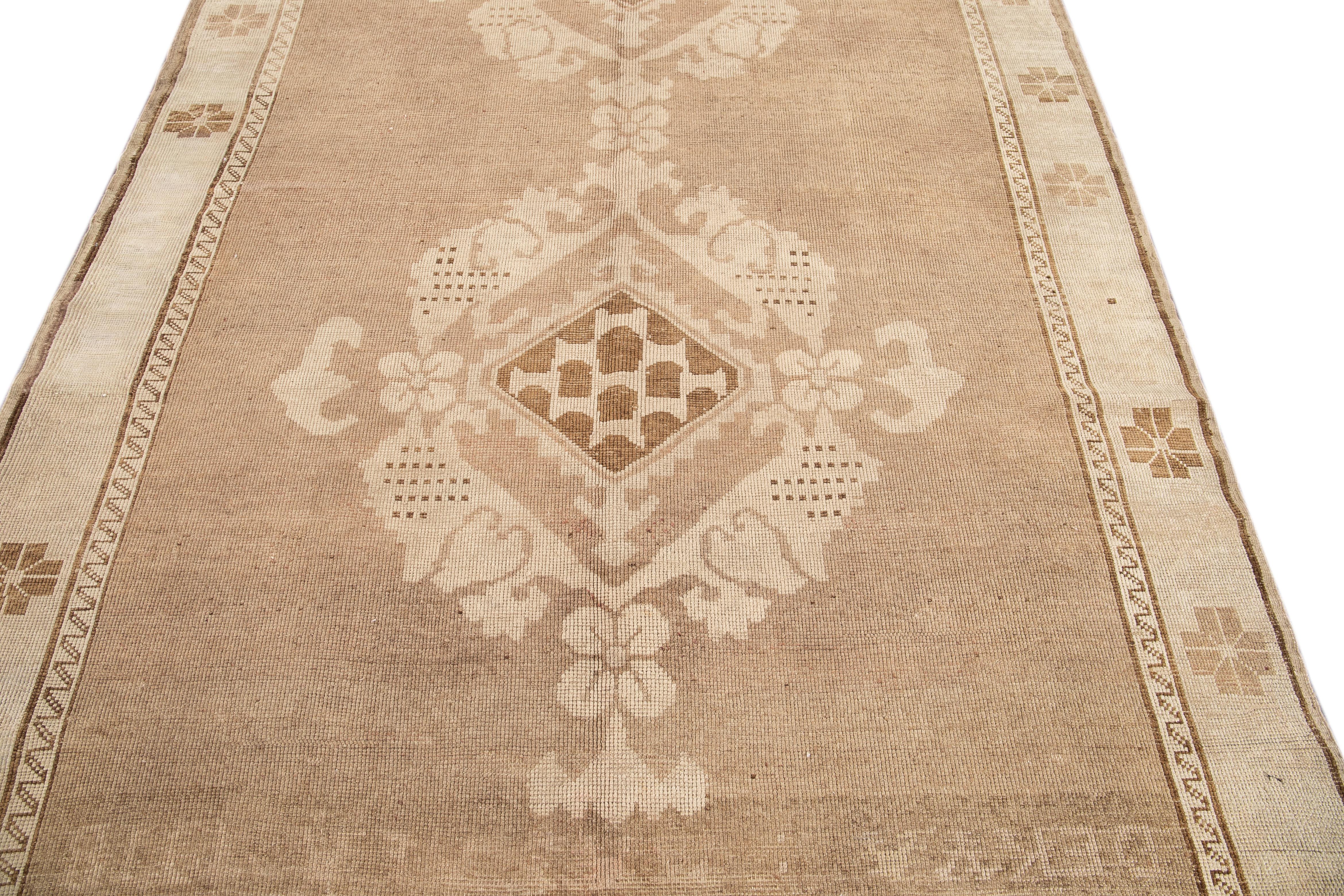 An Antique Khotan rug crafted from hand-knotted wool with an exquisite tan field, adorned with intricate ivory and brown accents in a dual medallion design spanning its entirety. This stunning piece is estimated to date back to the early