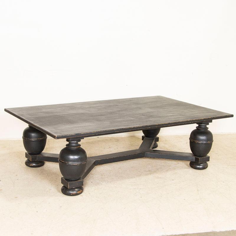 At almost 6' wide, this coffee table makes an impressive statement with large turned baroque legs and unique trestle base. While crafted around the turn of the century, it has been given a recent black painted finish for an updated modern look.