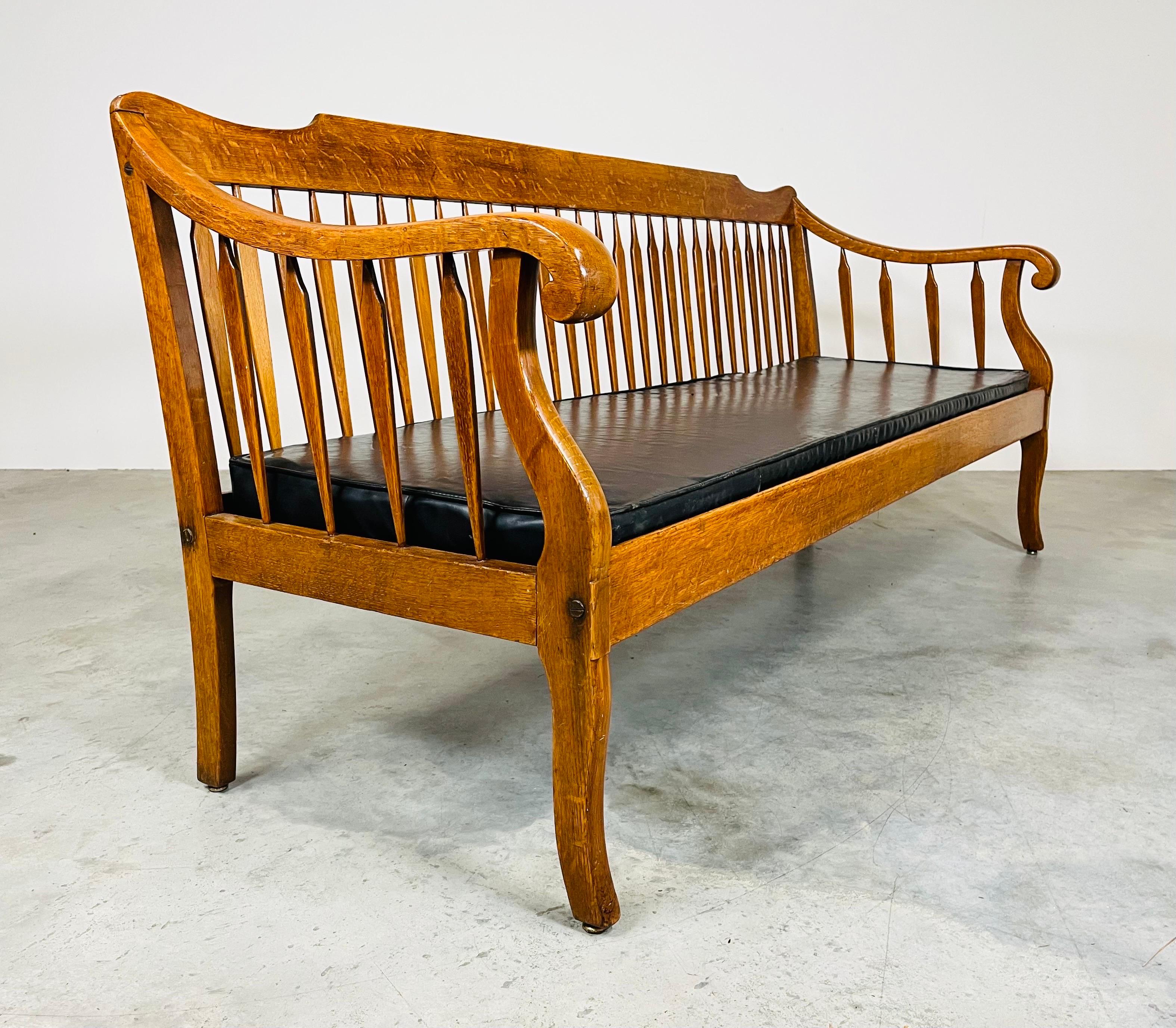 An especially handsome early 20th c. Lawyers bench of striking Tiger Oak with unusual arrow back & arms, heavy bronze as well as mortis & tenon joinery upholstered in black leather. The well constructed solid frame boasts an interesting combination