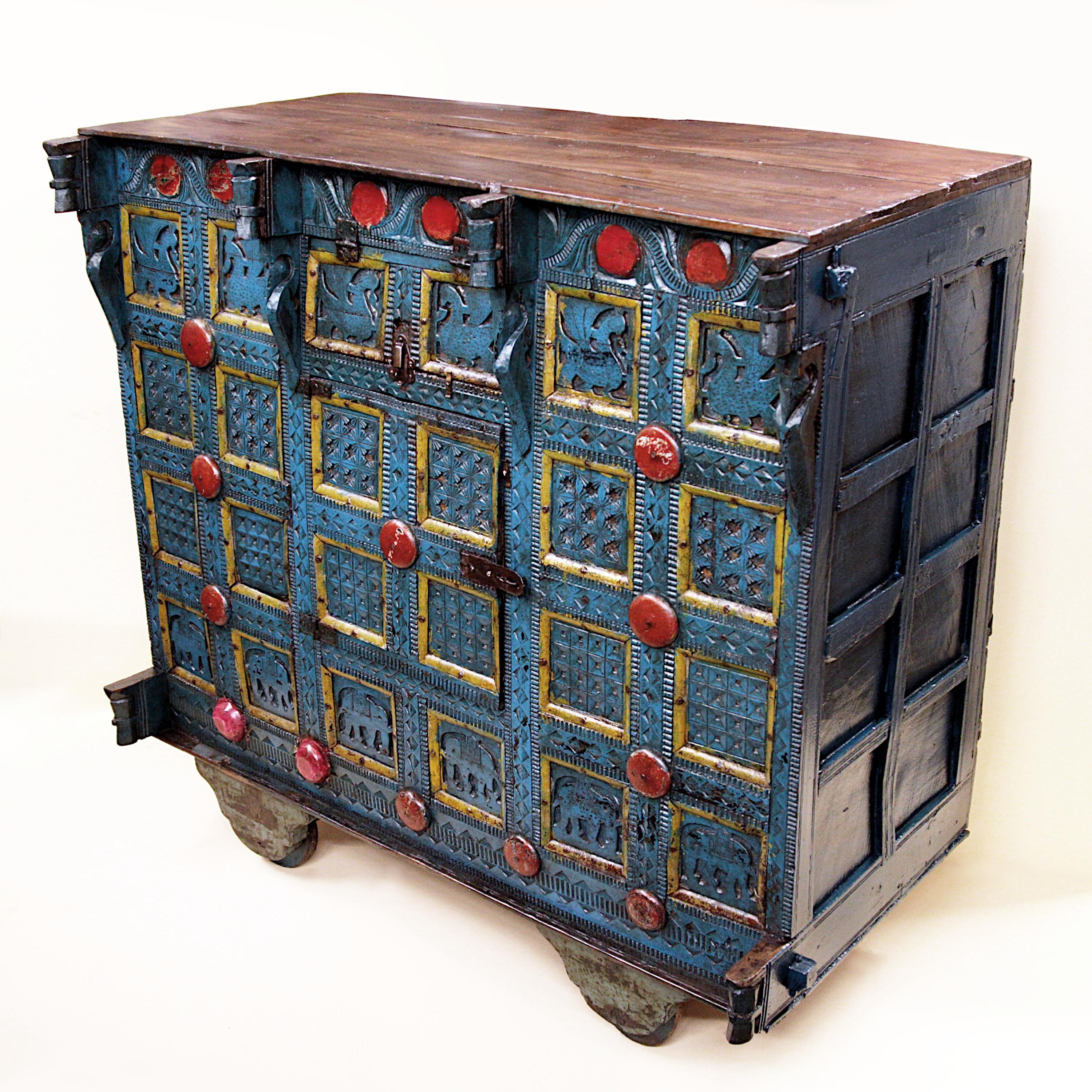 Wonderful early 20th century merchants chest/trunk. Chest features solid wood construction, ornately carved decoration, iron hardware, and wheels. Cabinet has been fully painted in bright, primary colors that beautifully accents the carving. With