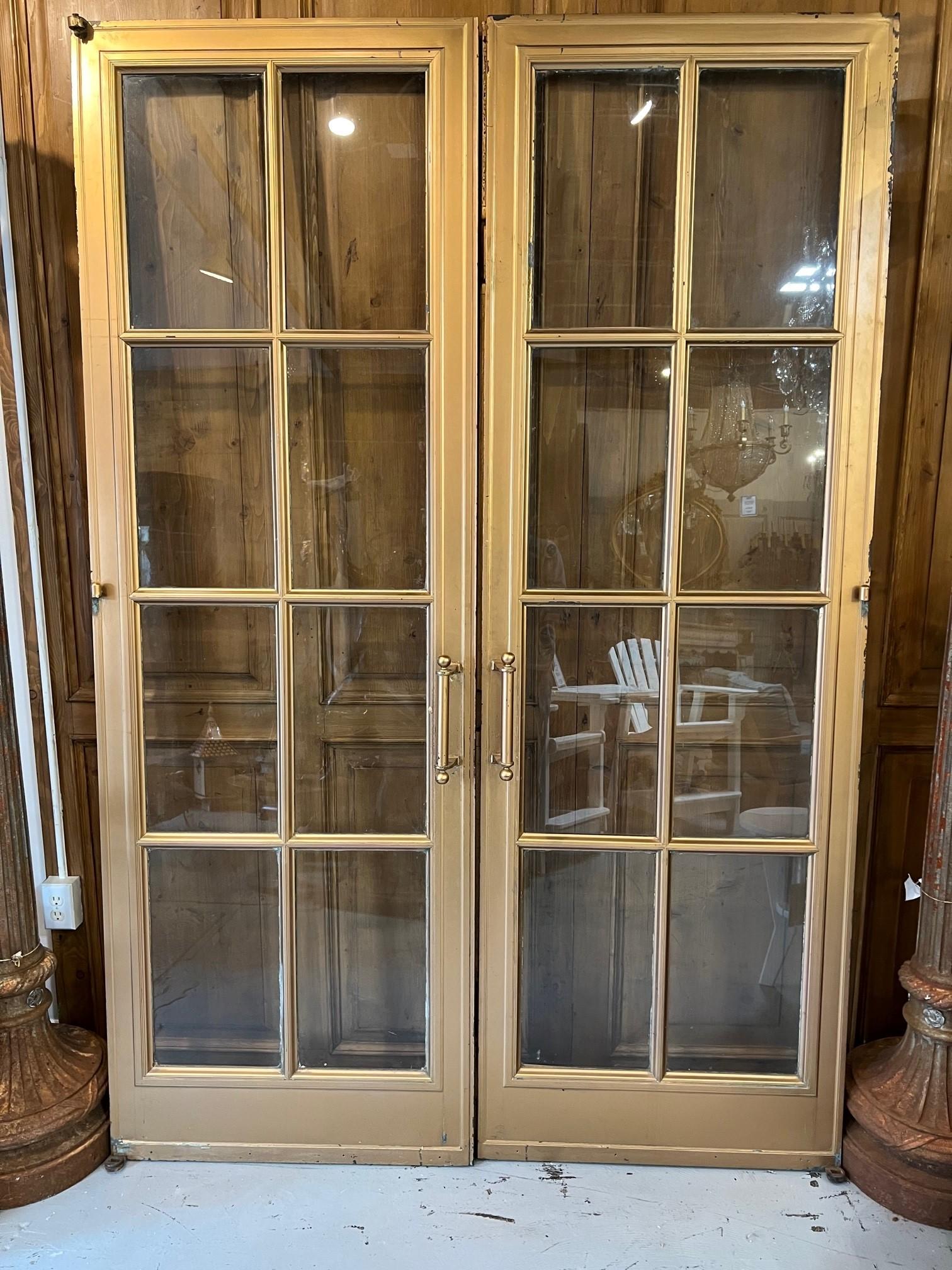 Amazing pair of antique bronze French doors with eight glass panels in each door. The doors are bronze with a gold painted finish, most likely from an large estate or commercial building. This is a great pair of doors which are very heavy and in