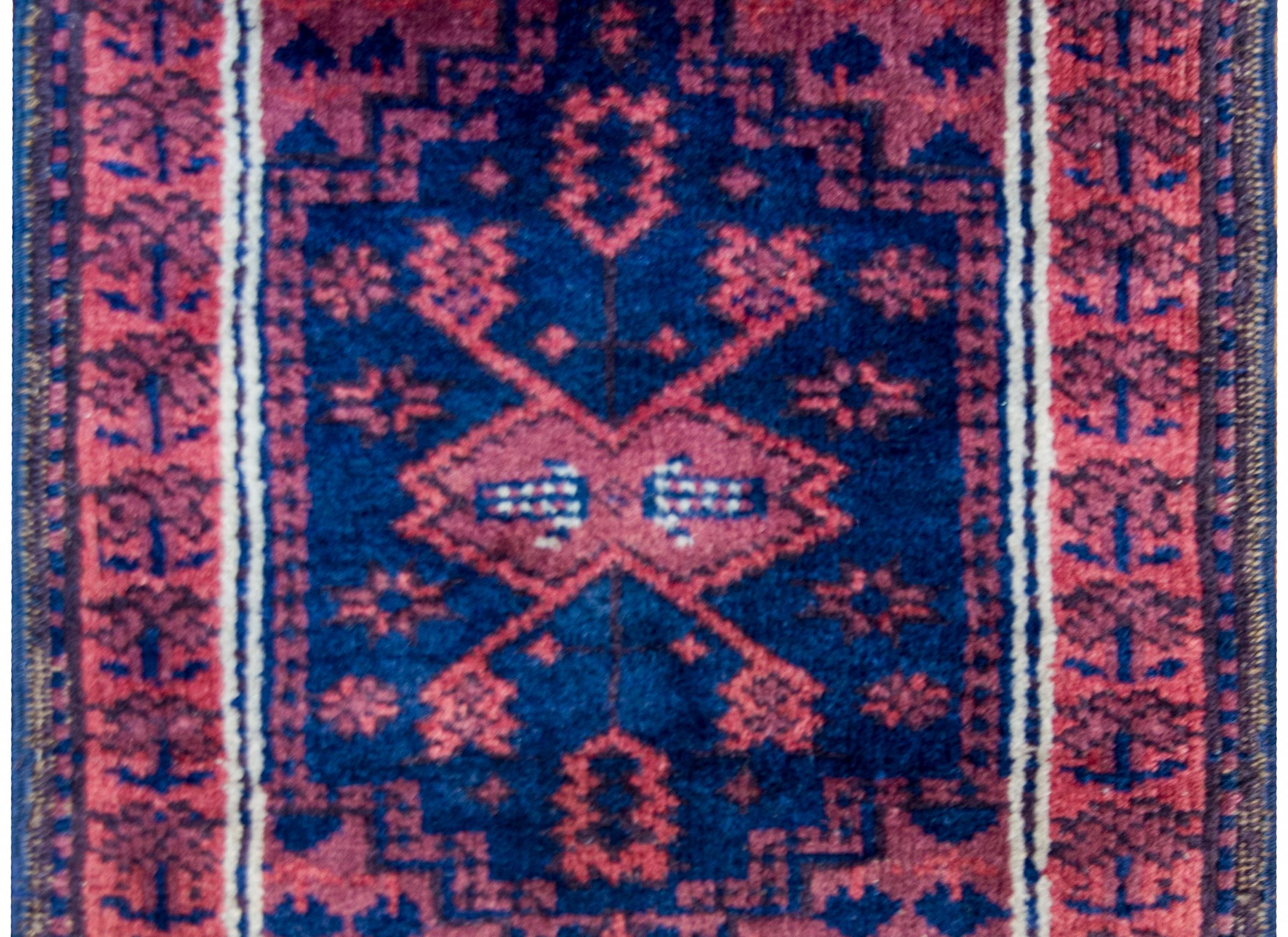 An early 20th century antique Persian Baluch rug with a beautiful central stylized cranberry floral medallion on an indigo background surrounded by a complementary cranberry floral border.