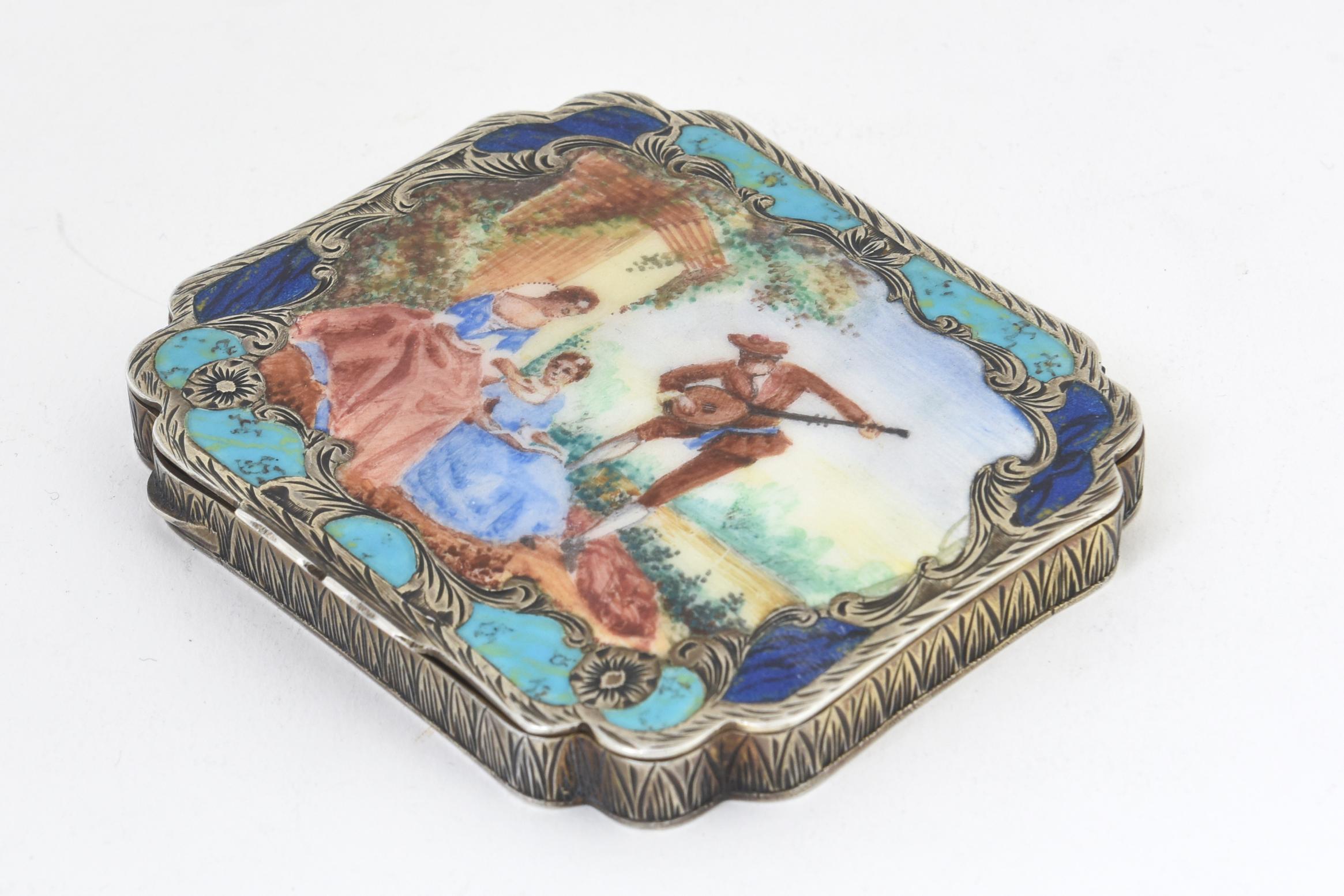Antique enamel and 800 silver compact. The rectangular top is enclosed by a rocaille scrollwork border with faux-lapis lazuli and faux-turquoise enamel inlay, centering a scene of a musician with two young women in a garden setting. Hand-chased