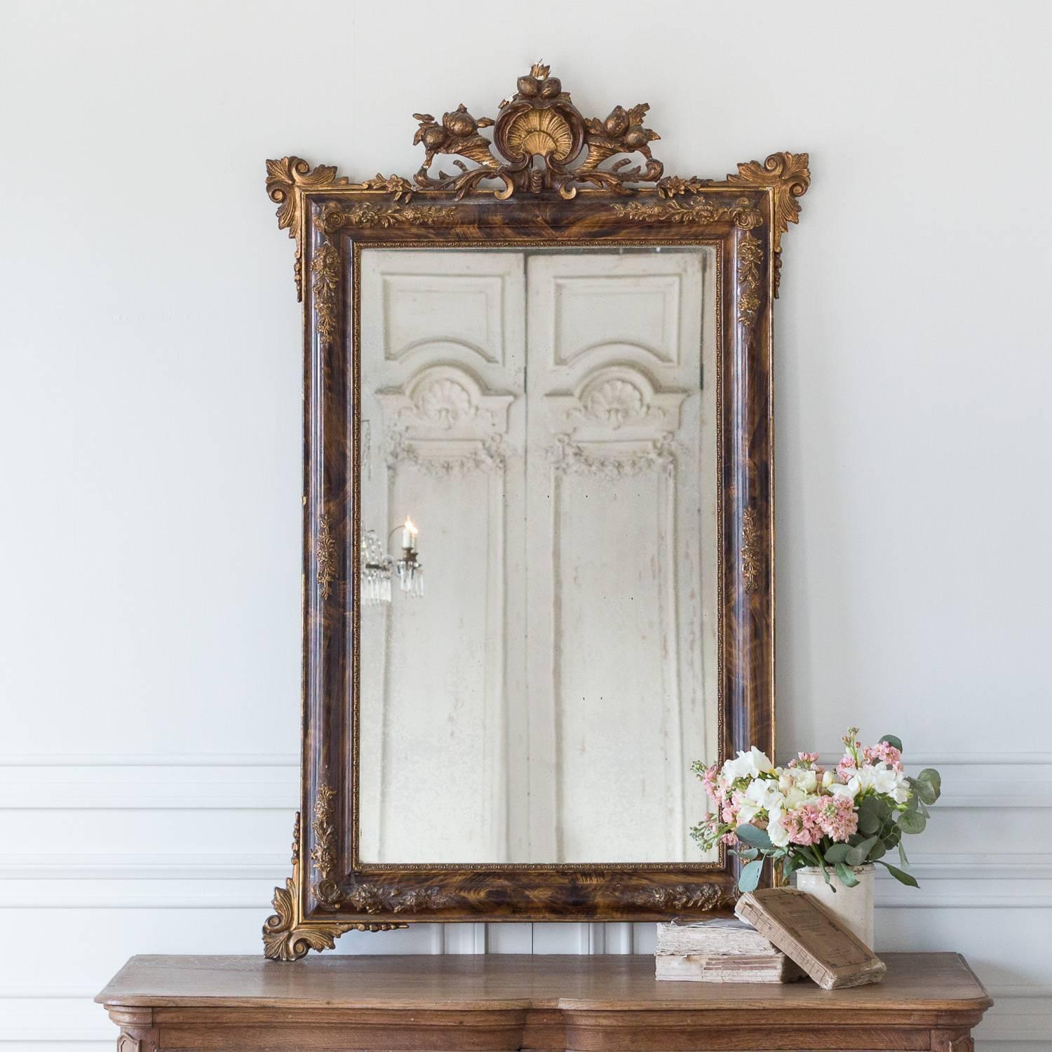 Antique mirror featuring an elaborately carved crest of a shell flanked by cornucopias spilling out fruit and flowers. The glass is perfectly worn with light stains detailing the age throughout the piece. The tortoise-stained wood and detailed