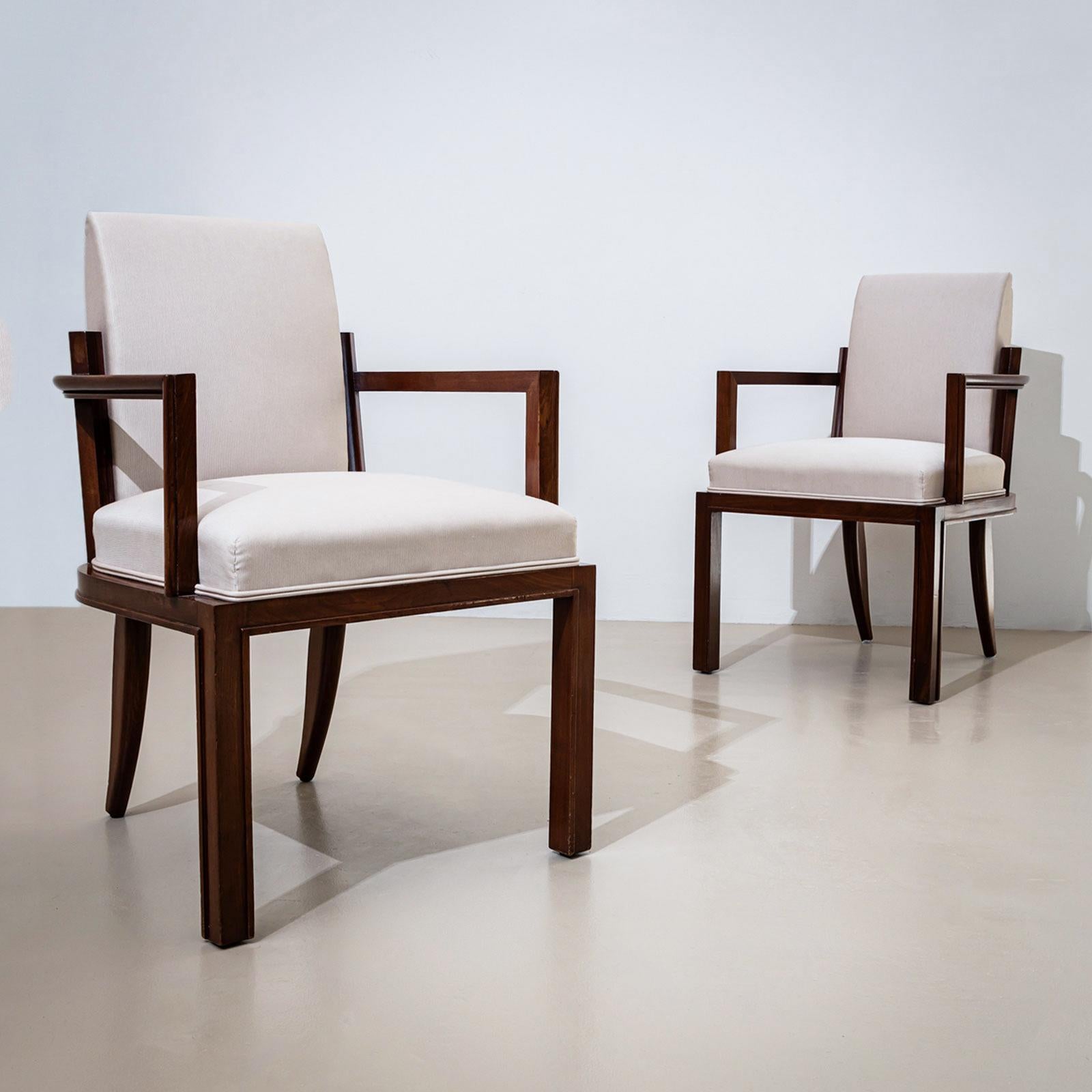 A pair of elegant Art Deco armchairs crafted from solid walnut. The edges of the legs are accentuated by a continuous trim, adding a refined detail to the design. The armrests are angled at right angles and terminate at a comfortable height,