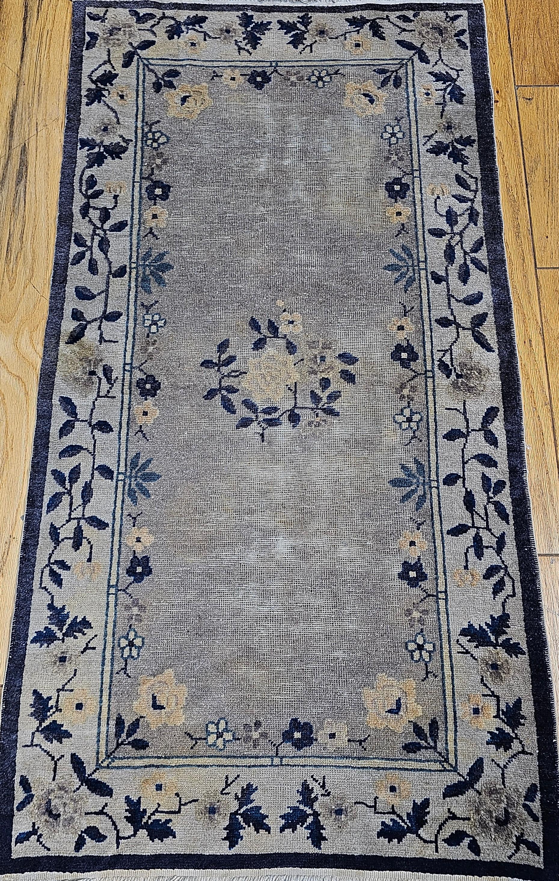 Vintage Art Deco Chinese area rug in earth tone colors and a beautiful floral design in gray, lavender, navy, and tan. The pile in the main field has worn down but the floral designs in the field and border have kept their wool giving a
