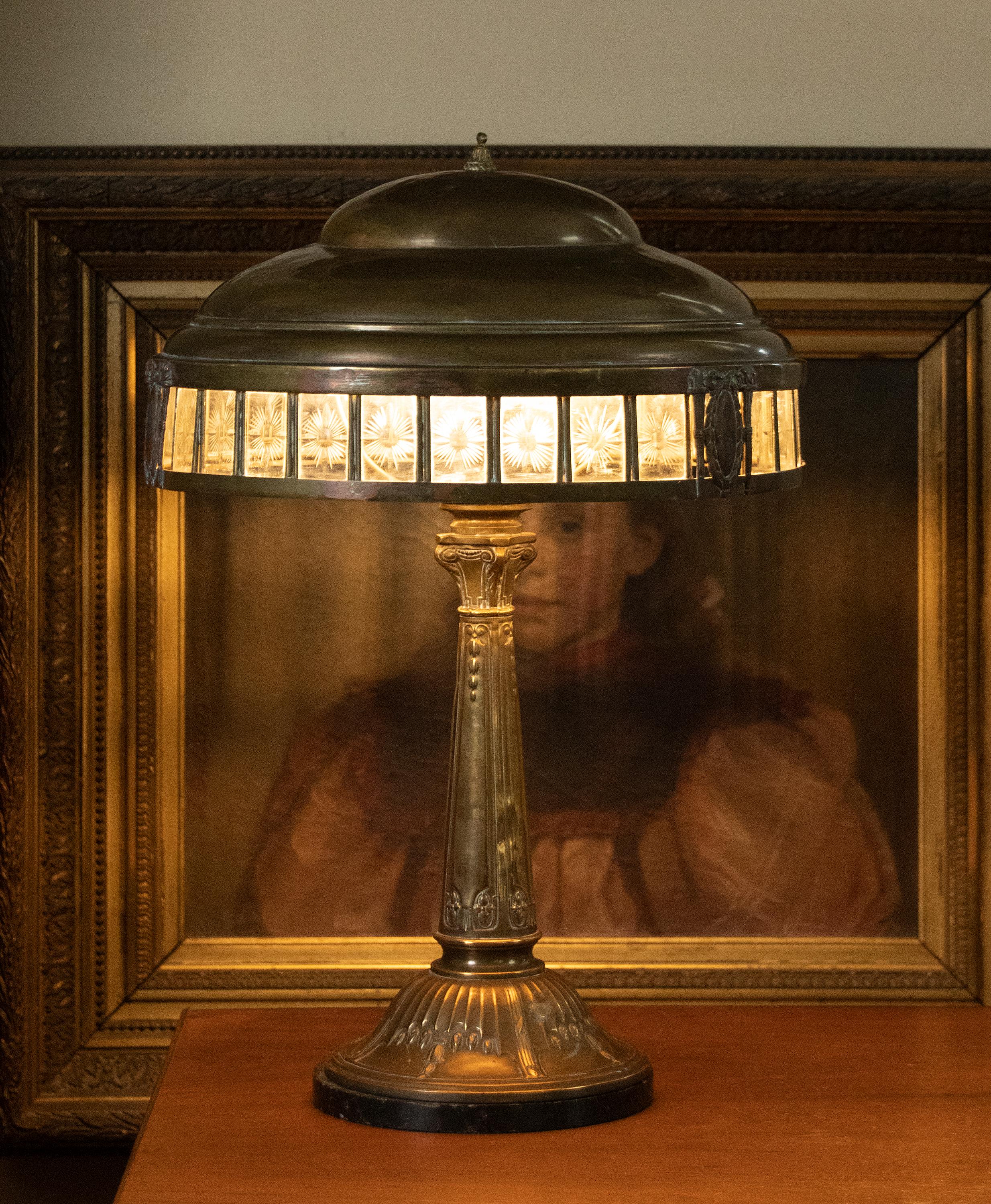 A brass table lamp from the French Art Deco period. The edge of the lampshade has cut glass, which gives a nice atmospheric effect when the lamp is swithed on. The shade rests on a brass base, with a black marble base underneath, so the lamp stands