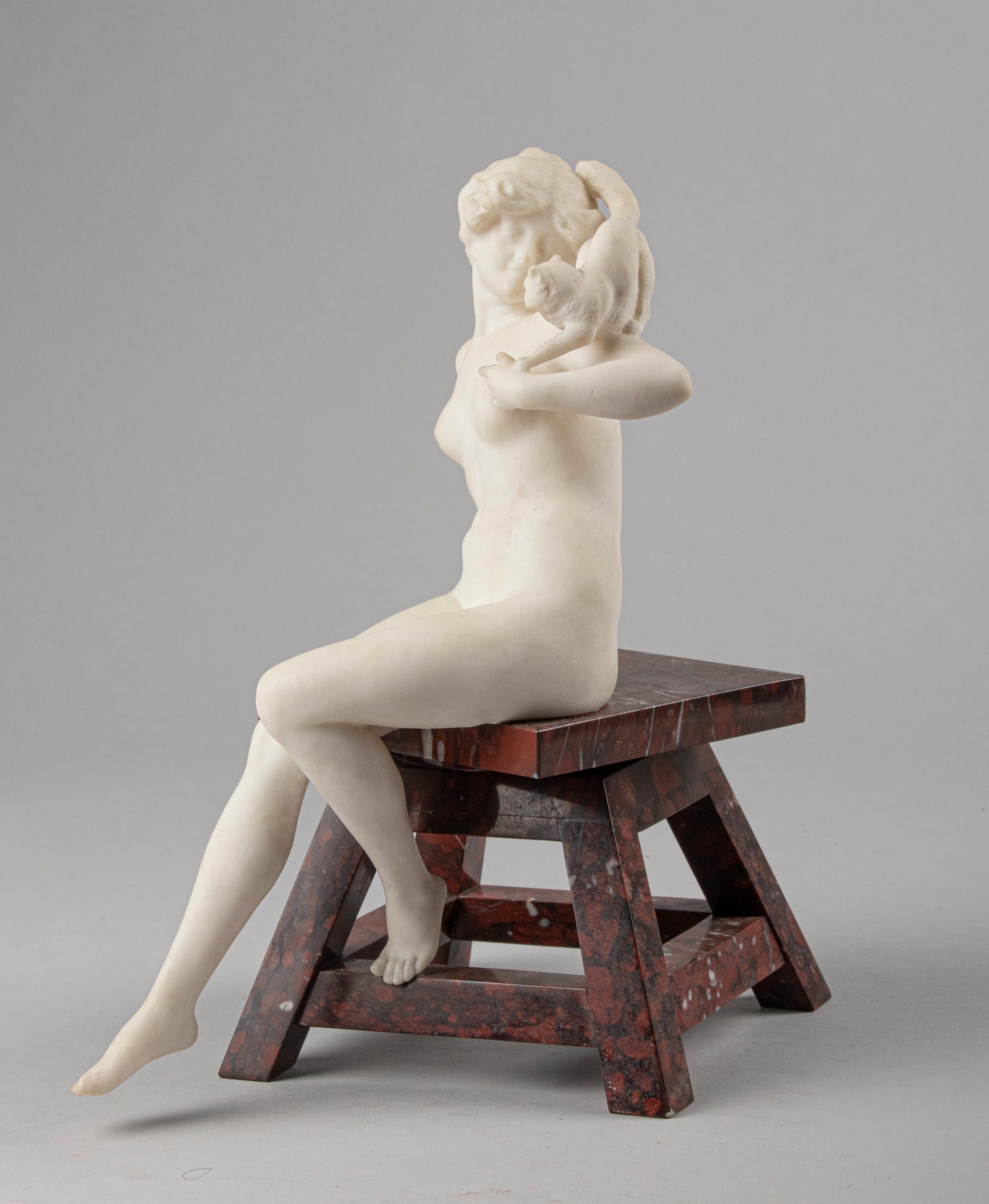 An elegant sculpture depicting a young woman with a cat on her shoulders. The statue is made of carara-marble and the stool is made of red marble 