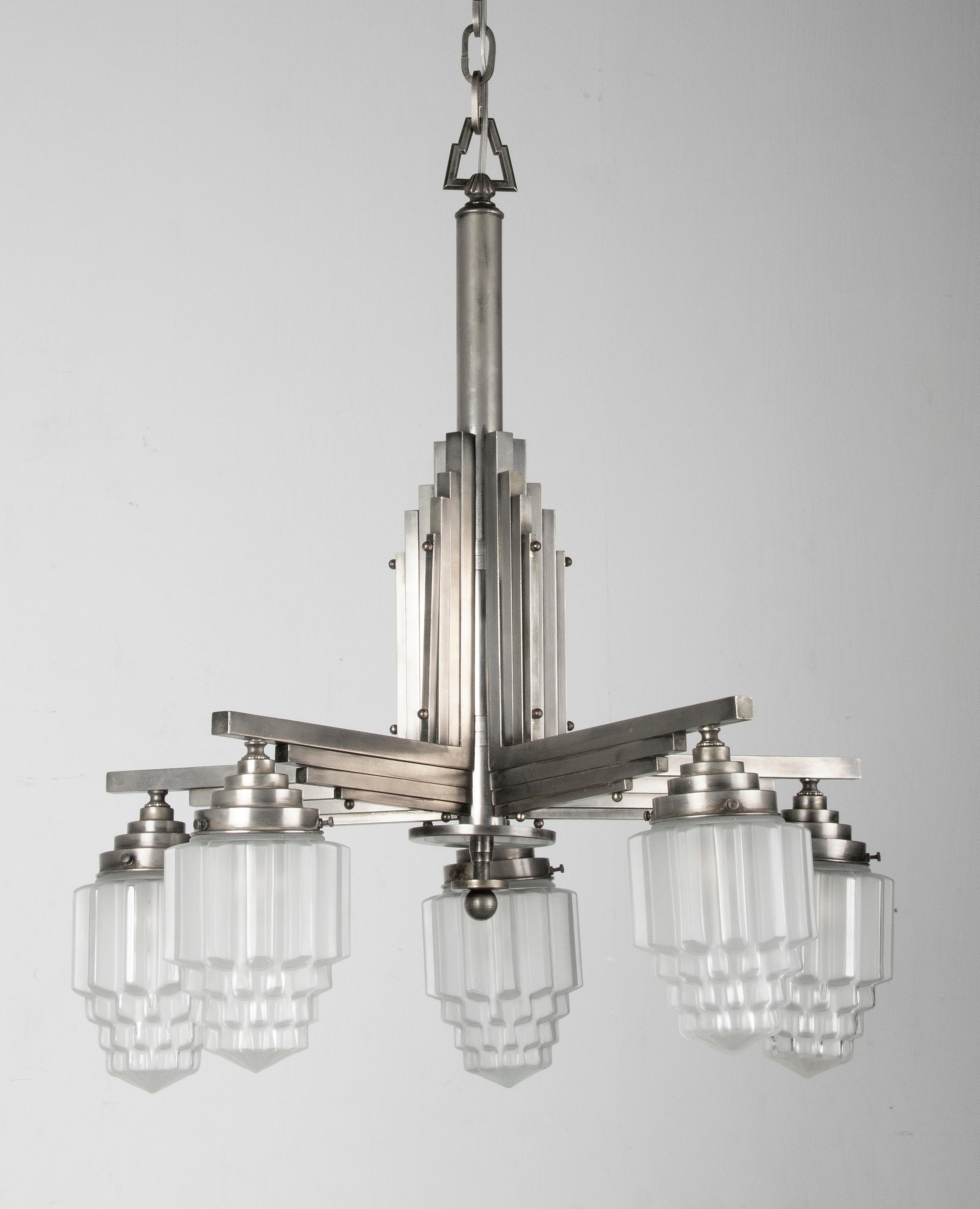 An Art Deco period Skyscraper chandelier made off metal. The molded frosted satin glass shades are also called Skyscraper model. The design is inspired by the Art Deco architecture, like the Empire State Building. The lamp has 5 light points with