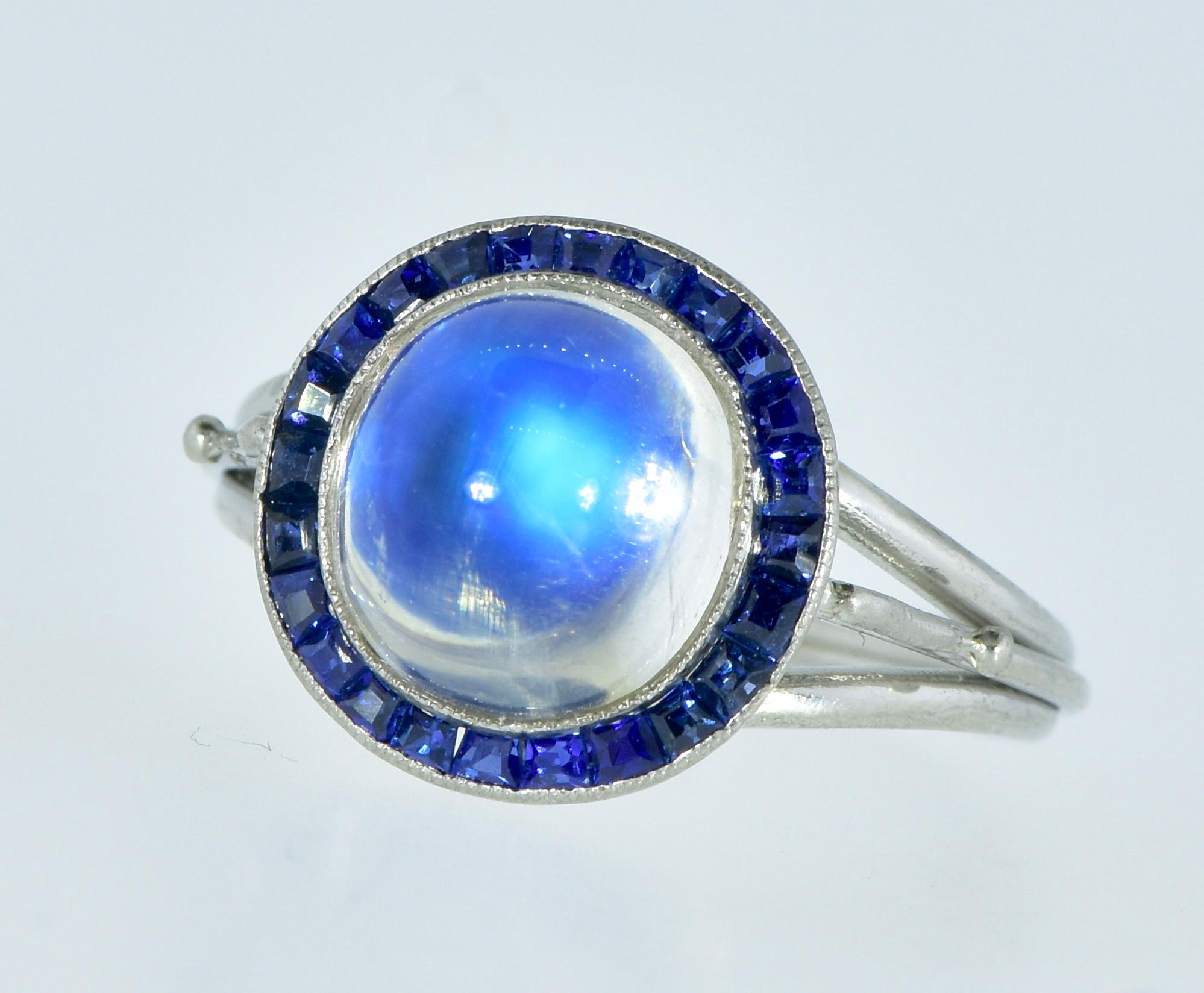 Fine moonstone probably from Burma or Ceylon, weighing an estimated 5.5 cts., displaying a blue hue, this high cabochon is encircle by natural vivid blue sapphires.  The 23 sapphires are well cut and well matched, they are estimated to weigh 1.38