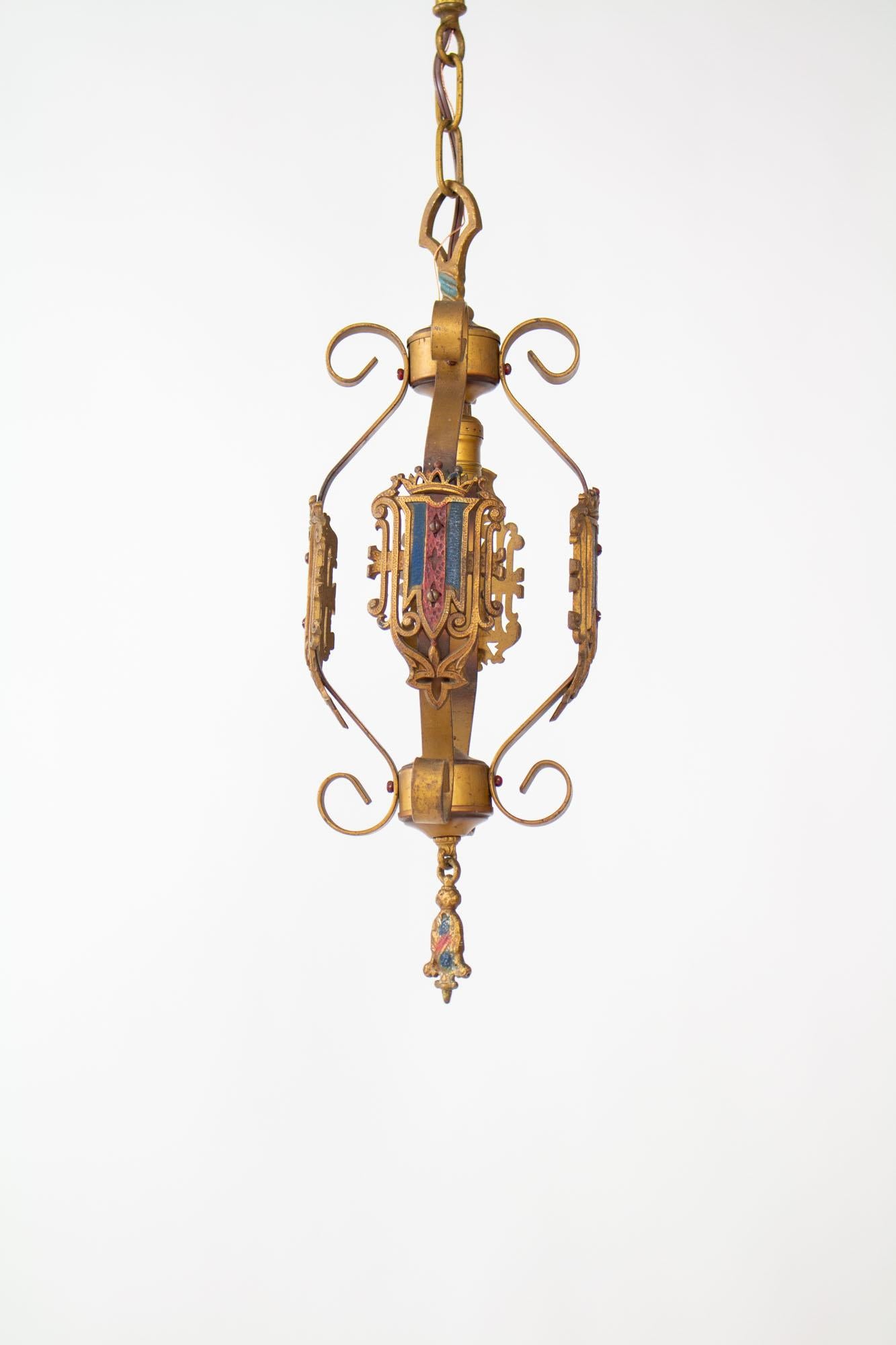 Early 20th Century pendant. Antique gold finish with original blue accents. Central light in a cage formed from four bent arms with shields.

20” tall pendant only