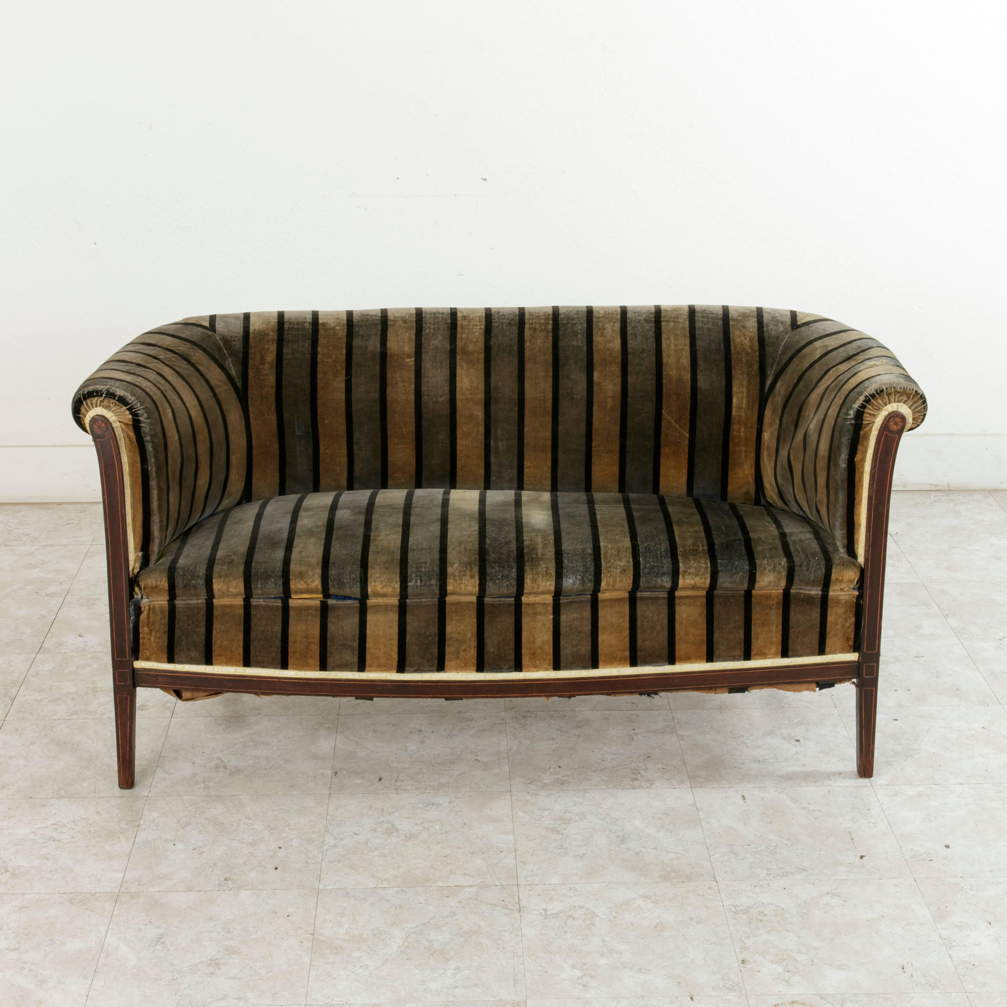 A rare find in French Art Deco period pieces! This chic small-scale settee or sofa has the Classic lines of the furniture of the period but is set apart by its unusual details. Its mahogany frame is inlaid with lemon wood and sycamore rosettes on
