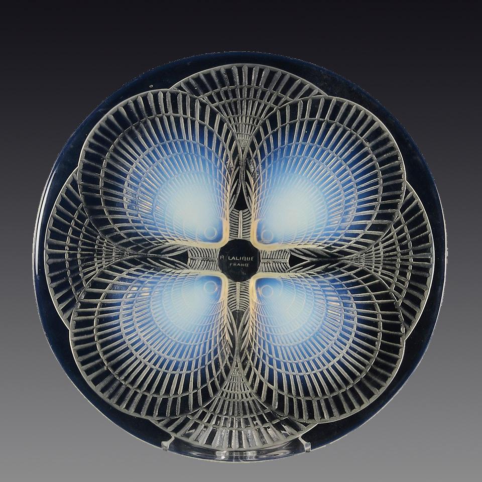 Un piatto in vetro francese Art Déco dei primi del Novecento, con superficie smerigliata e motivo geometrico inciso e conchiglie a smerlo in rilievo, dal colore opalescente blu cielo intenso, firmato R Lalique.

Coquilles No.1
Numero di catalogo: