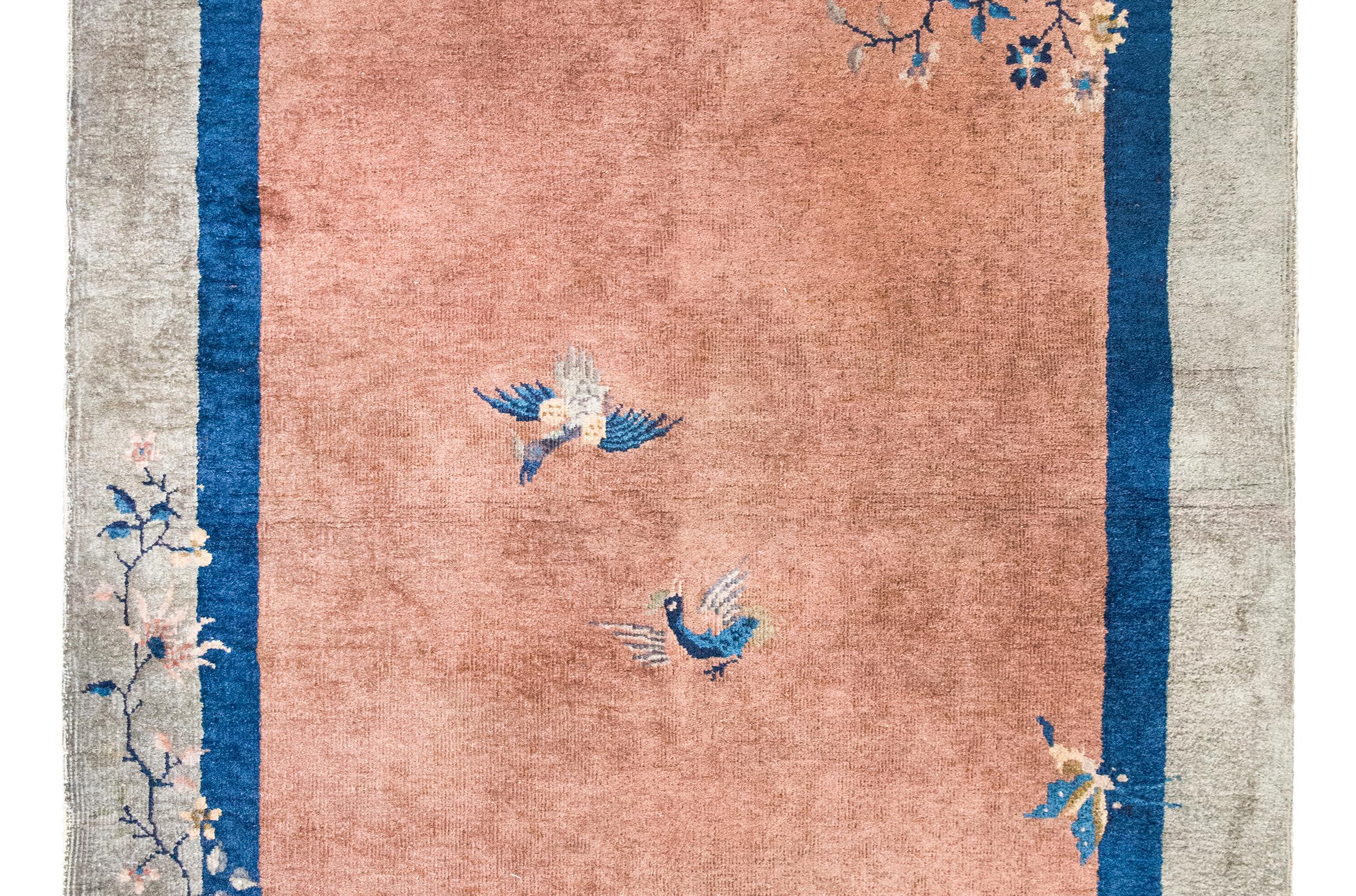 Cautivadora alfombra Art Decó china de principios del siglo XX, esta pieza es una magistral mezcla de simbolismo y color. El suave campo de color melocotón está enmarcado por una fina franja azul marino y un ancho borde gris, creando un refinado