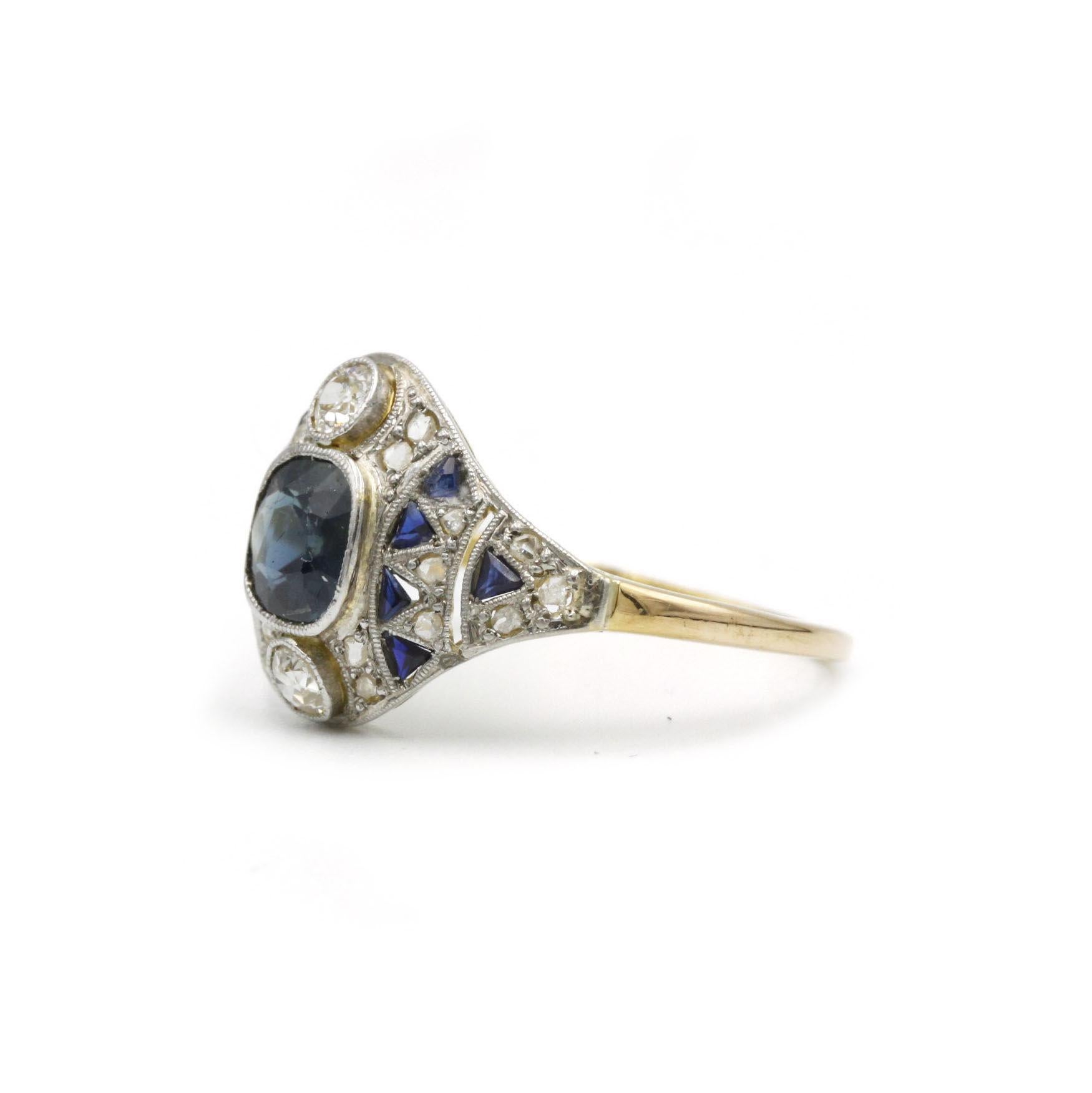 A striking example of Art Deco craftsmanship, this early 20th Century ring pairs a deep-blue, 0.90 ct sapphire with an architectural halo of 22 brilliant-cut diamonds (totaling ~0.35 ct) and 10 calibré-cut sapphires (~0.20 ct). Rendered in rich 18 K