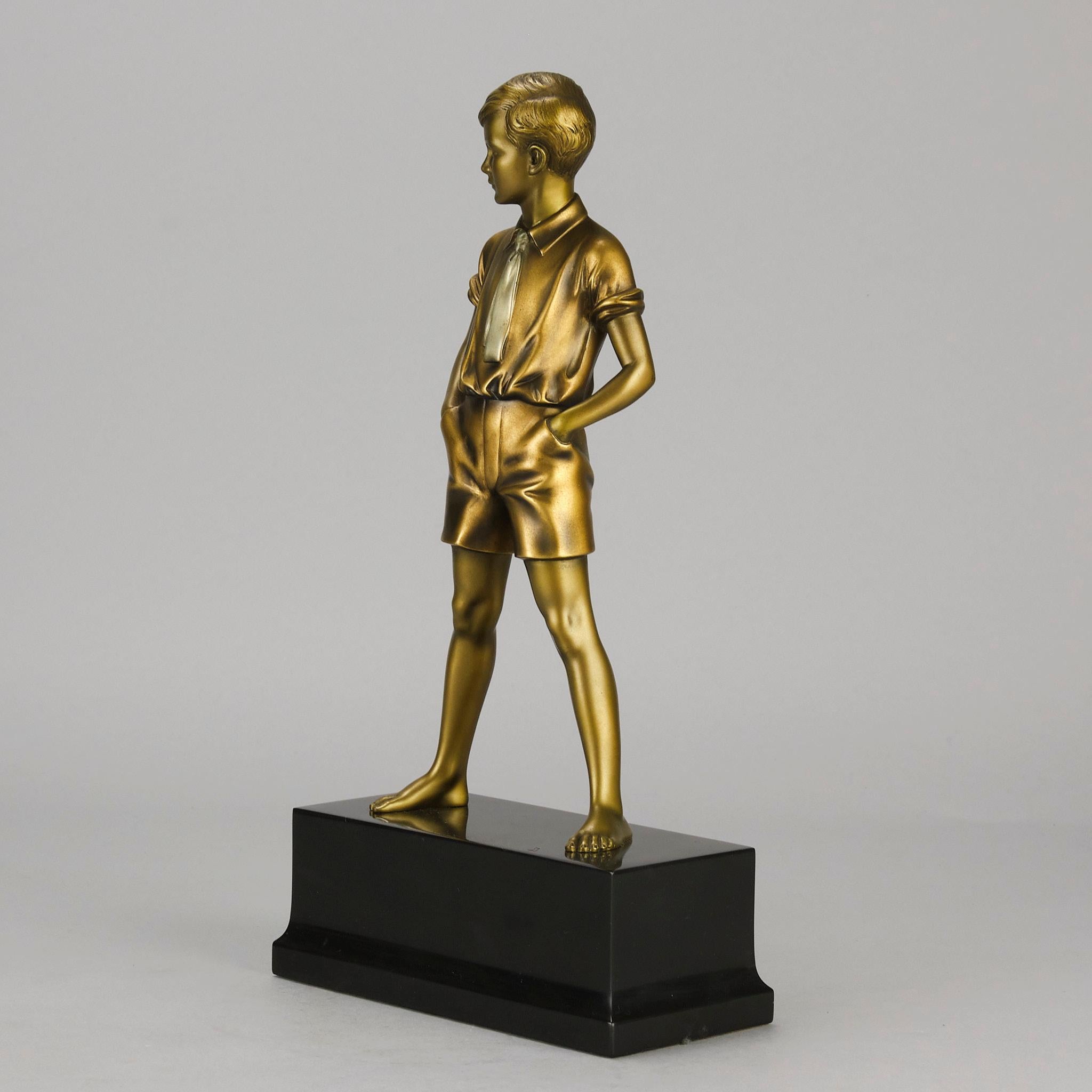 Excelente figura de bronce pintado en frío Art Decó de principios del siglo XX de un joven con pantalones cortos que sostiene un libro bajo el brazo con las manos en los bolsillos. El bronce tiene un excelente color dorado pintado en frío y se alza
