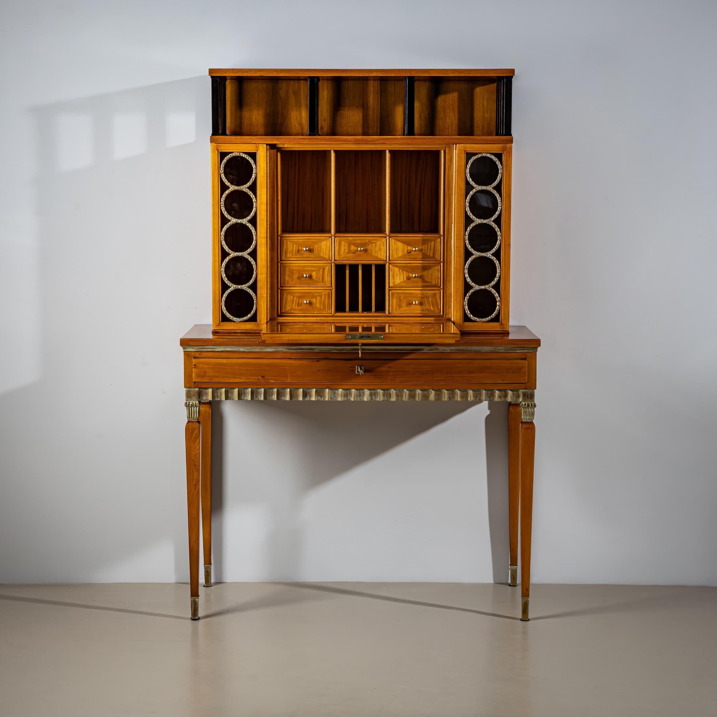 Elegant Art Deco secretaire, likely of Scandinavian origin, dating to the 1920s. Raised on tall, tapering legs with patinated capitals and brass sabots, the piece features a wide drawer with a finely carved wave-patterned frieze. The upper section
