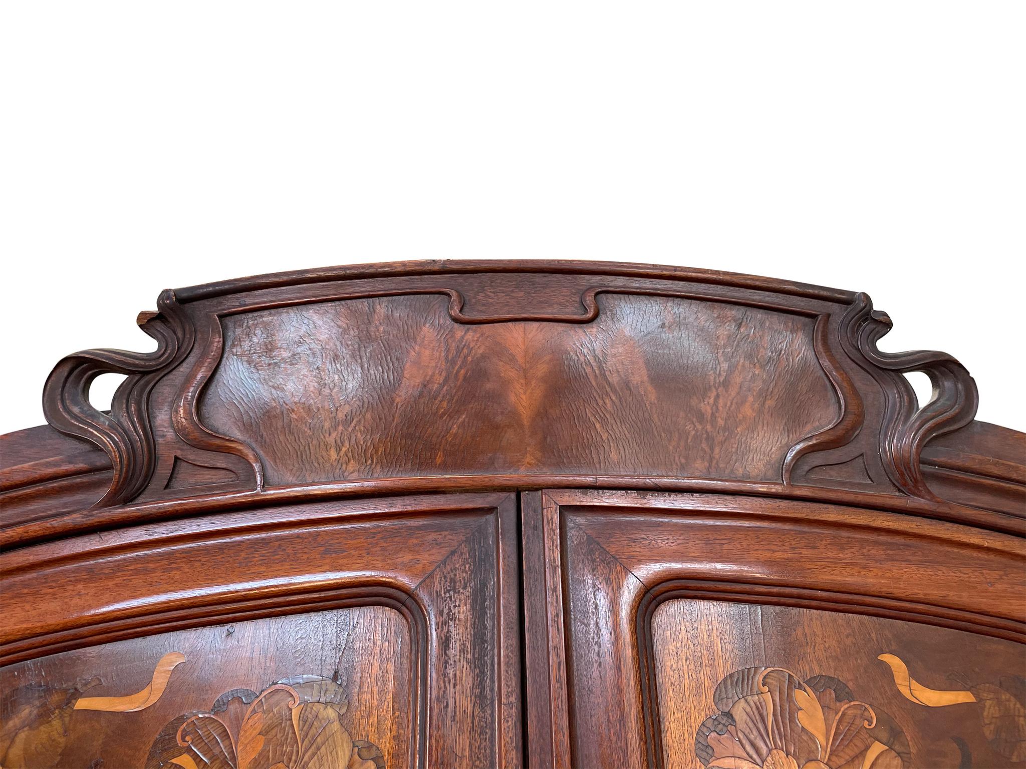 This two-door mahogany wardrobe was handcrafted in the 1900s. It has a beautiful floral inlay design framed by a curved molding that is characteristic of Art Nouveau. The wood has aged beautifully. It is a warm red-brown with a rich grain. Inside is