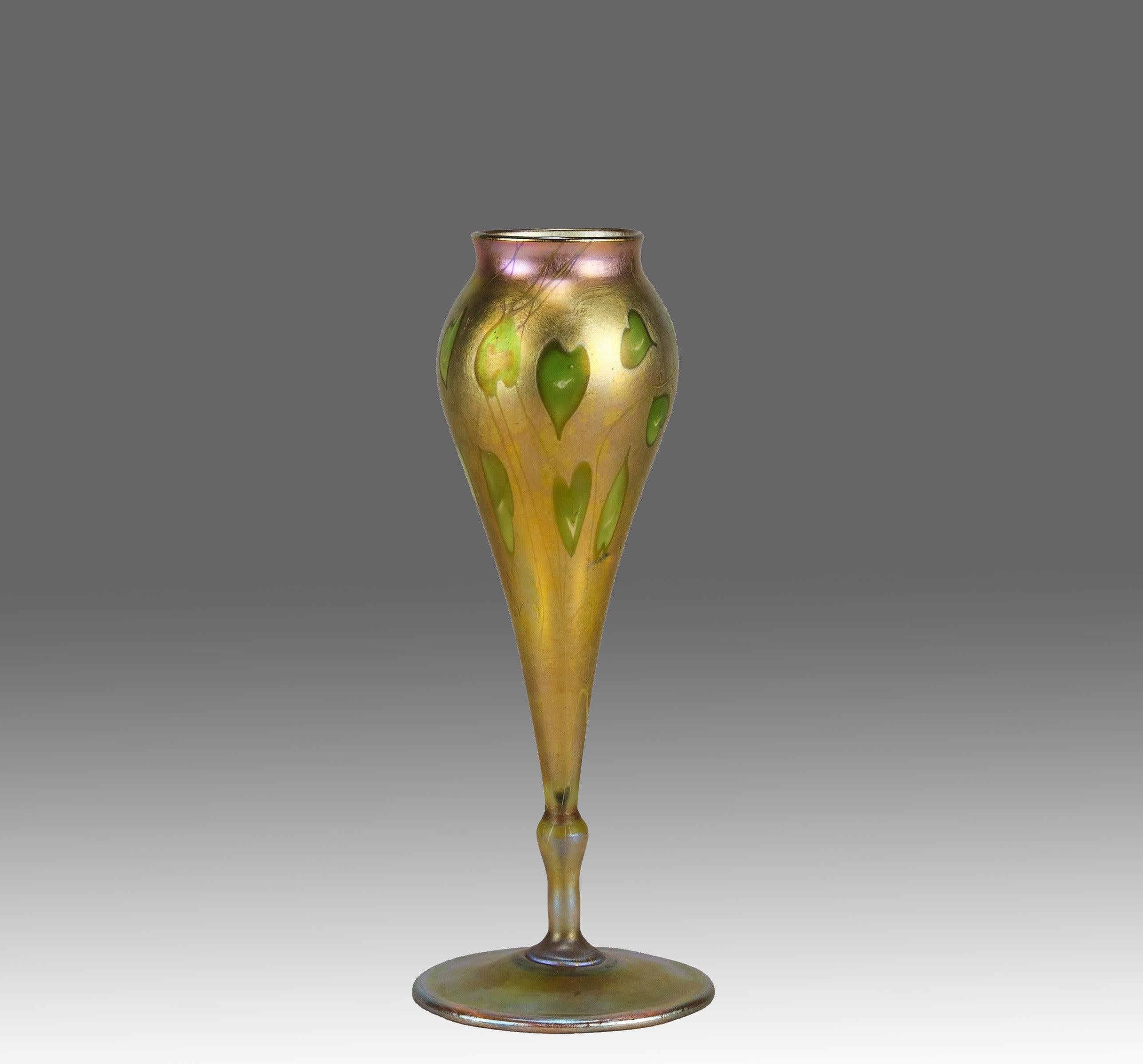 Un imponente vaso in vetro iridescente americano dei primi del Novecento dalla forma slanciata con cuori verdi che brillano attraverso un'attraente iridescenza dorata, firmato A.L.C. Tiffany Favrile e numerato alla base.

INFORMAZIONI