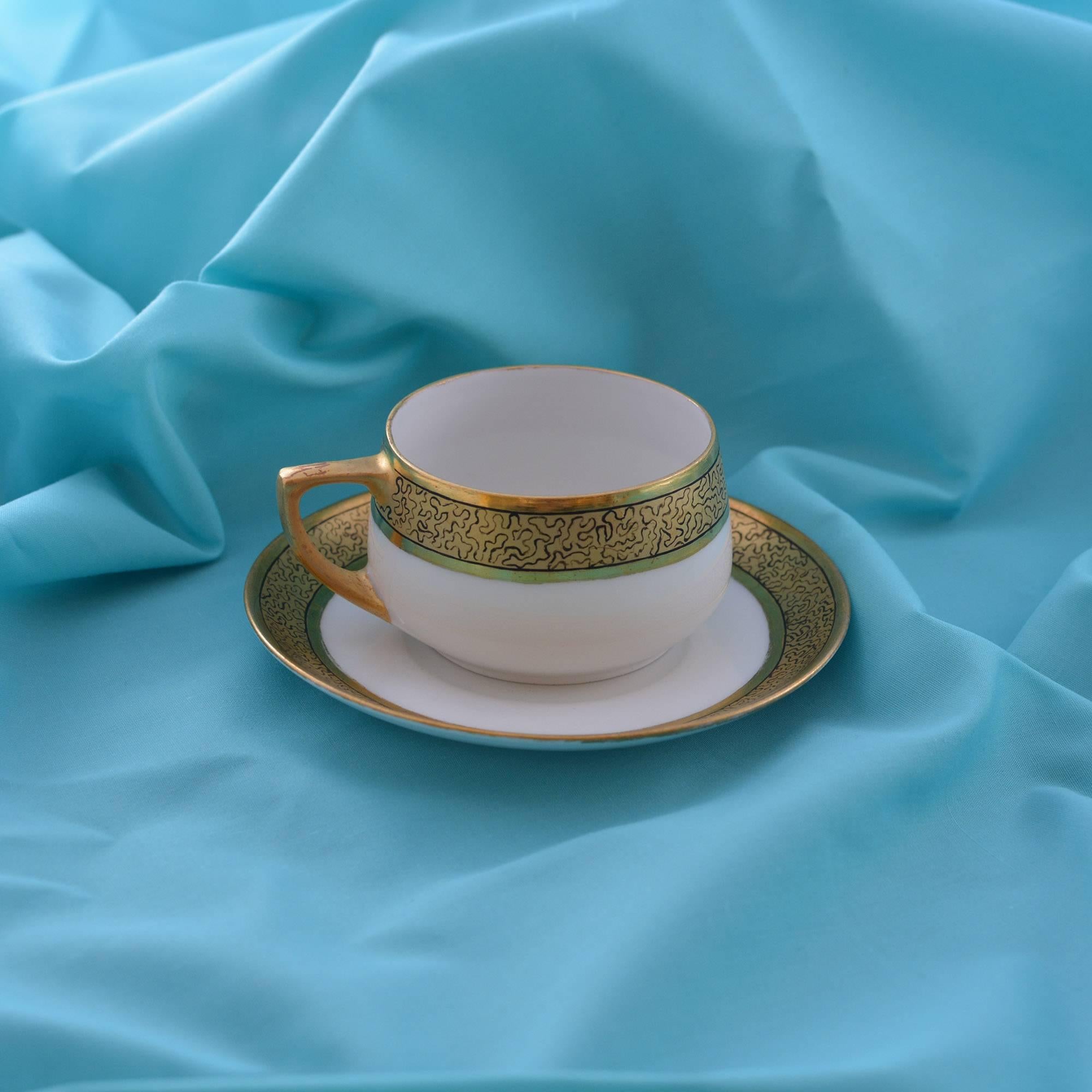 This fine porcelain Art Nouveau style cups with saucers have a wide gilded band to the rims with a delicate black line design within and the saucers have gilded trim. The group is comprised of eight saucers, a creamer and eight cups. They bear a