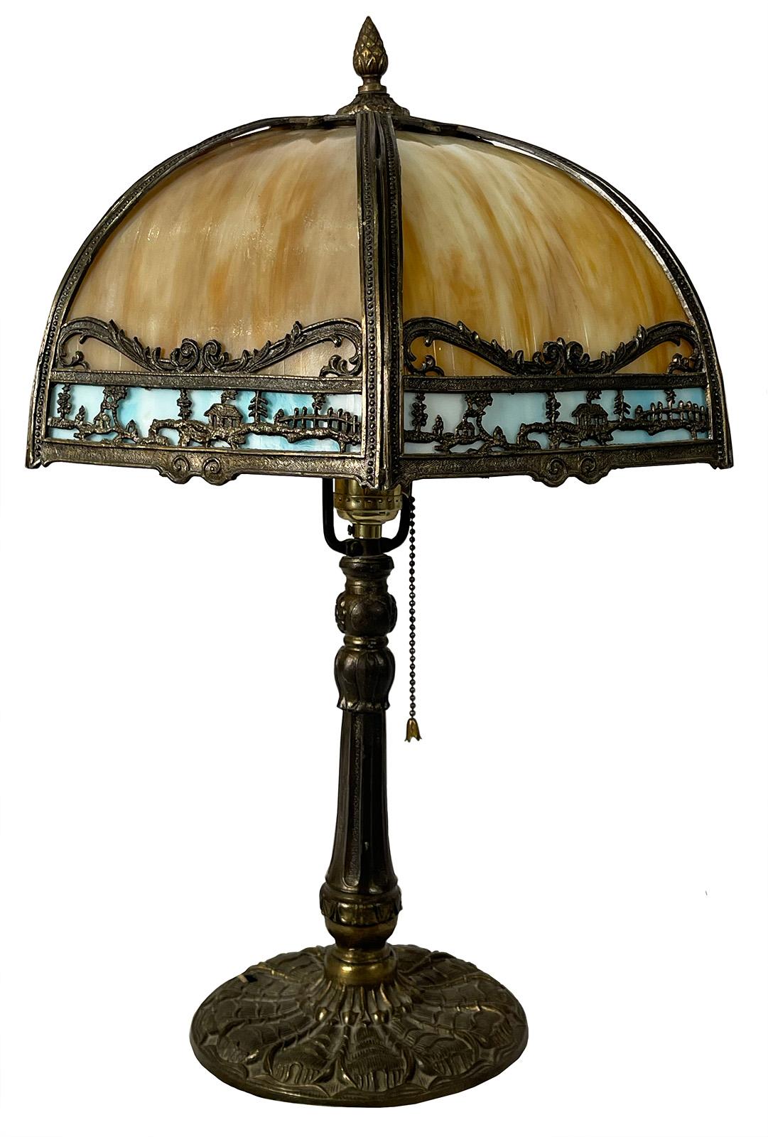 An early 20th century Art Nouveau style table lamp made with blue and yellow slag glass with a bronze cottage scene motif.

Dimensions: 21