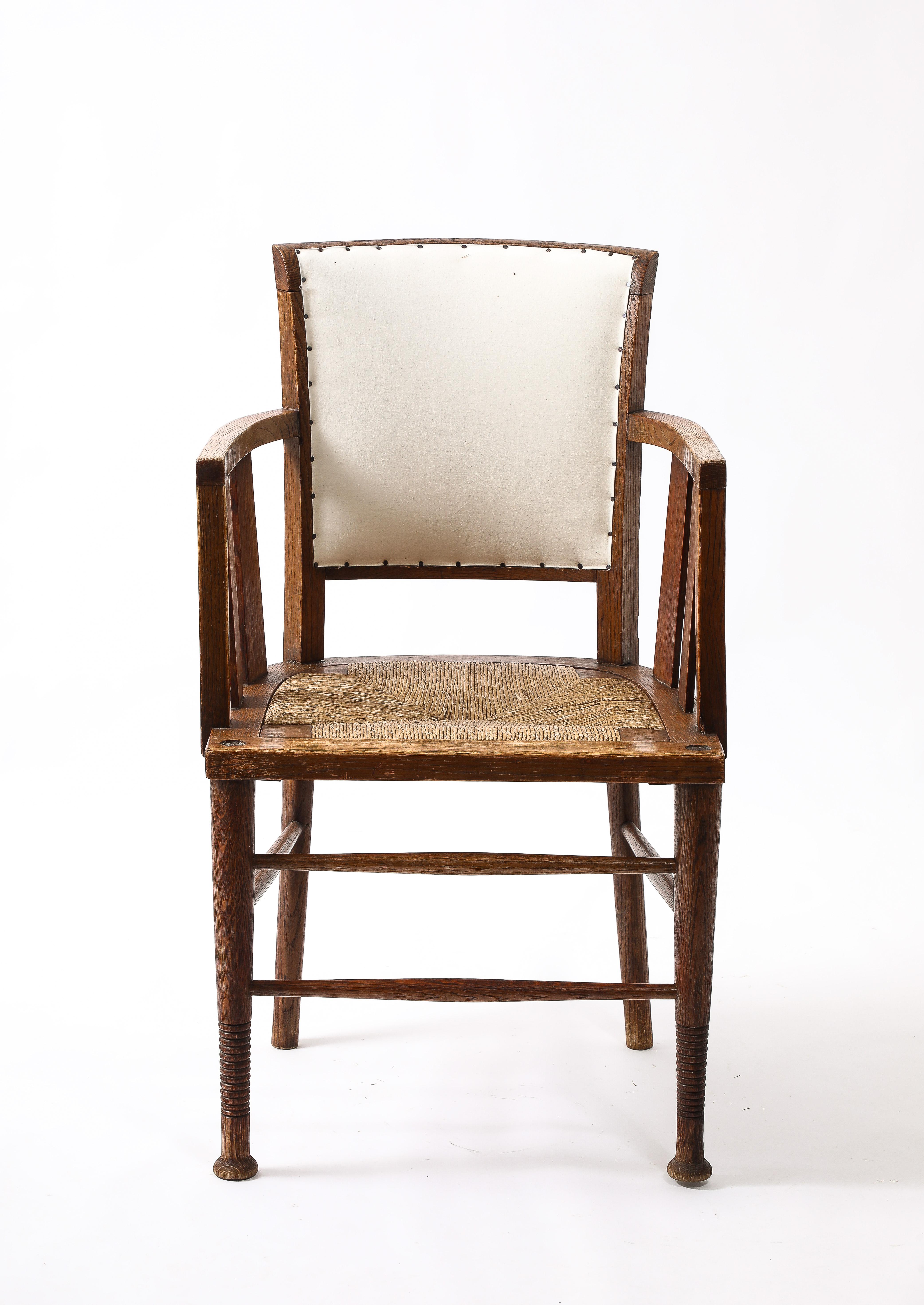 Early 20th century Arts and Crafts armchair, constructed in oak with the original drop-in rushed seat. Good quality with interesting design details and great form. Re-covered in calico.