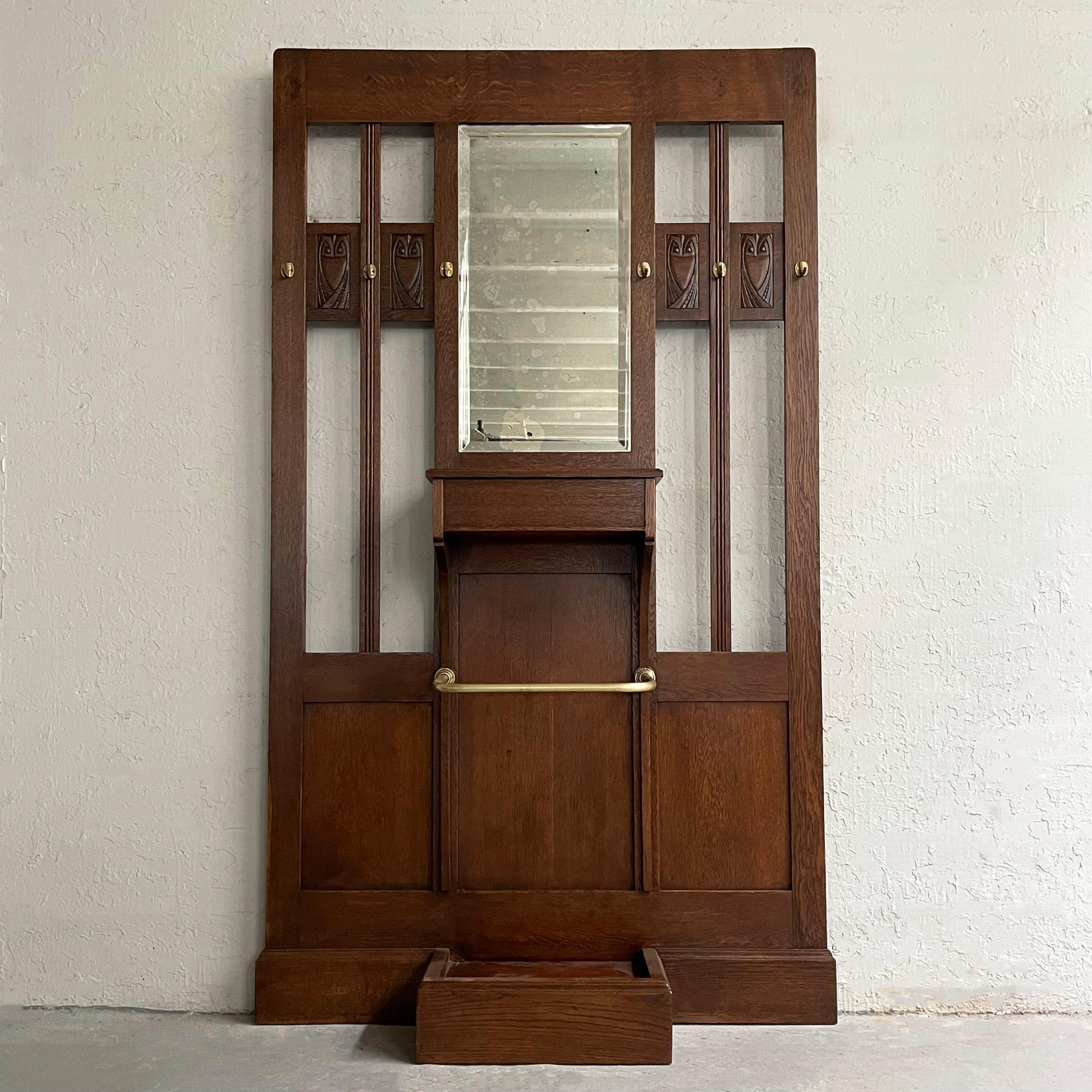 Early 20th century, arts and crafts, oak, entryway hall tree with carved owl motif features a beveled mirror with storage box and brass hooks and umbrella stand bar.