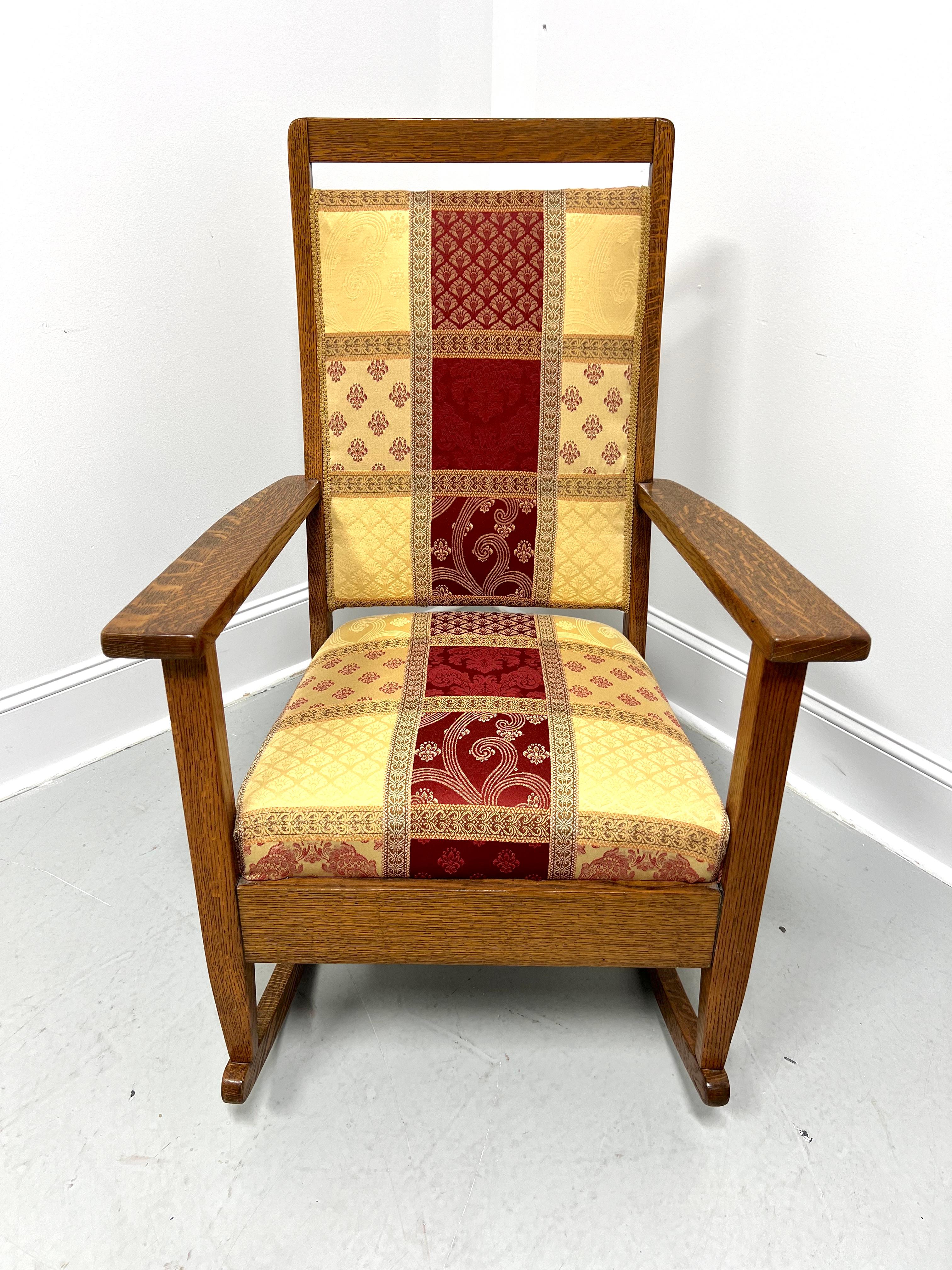 An Arts & Crafts period upholstered rocking chair, unbranded. Solid quartersawn tiger oak, raised solid crestrail, upholstered backrest & seat in a red, beige, & gold color plaid-like fabric, flat arms with square supports, solid broad apron,