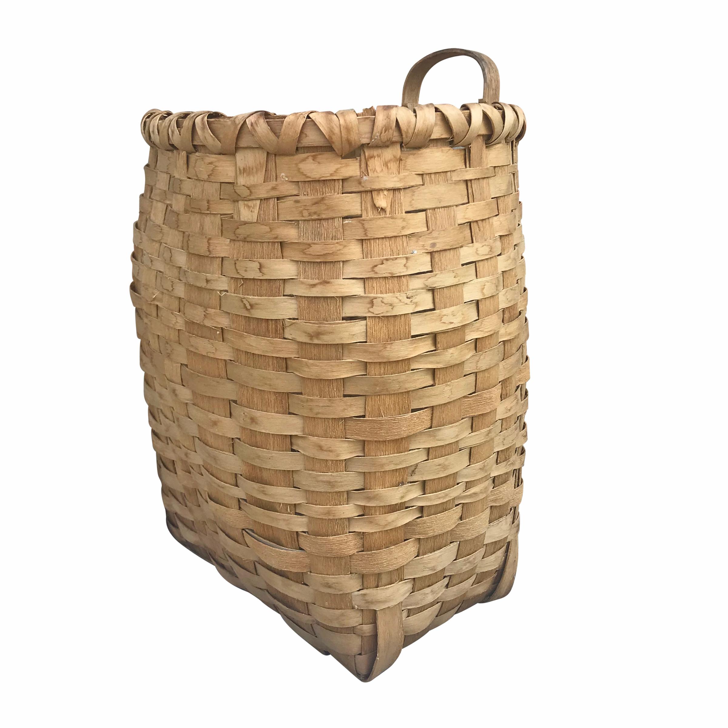 A sweet early 20th century handwoven ash splint gathering basket with an ovoid opening, a square base, a double banded rim, and one bentwood handle on the back. This basket was found in Northern Michigan. It's a lovely basket that can hang against