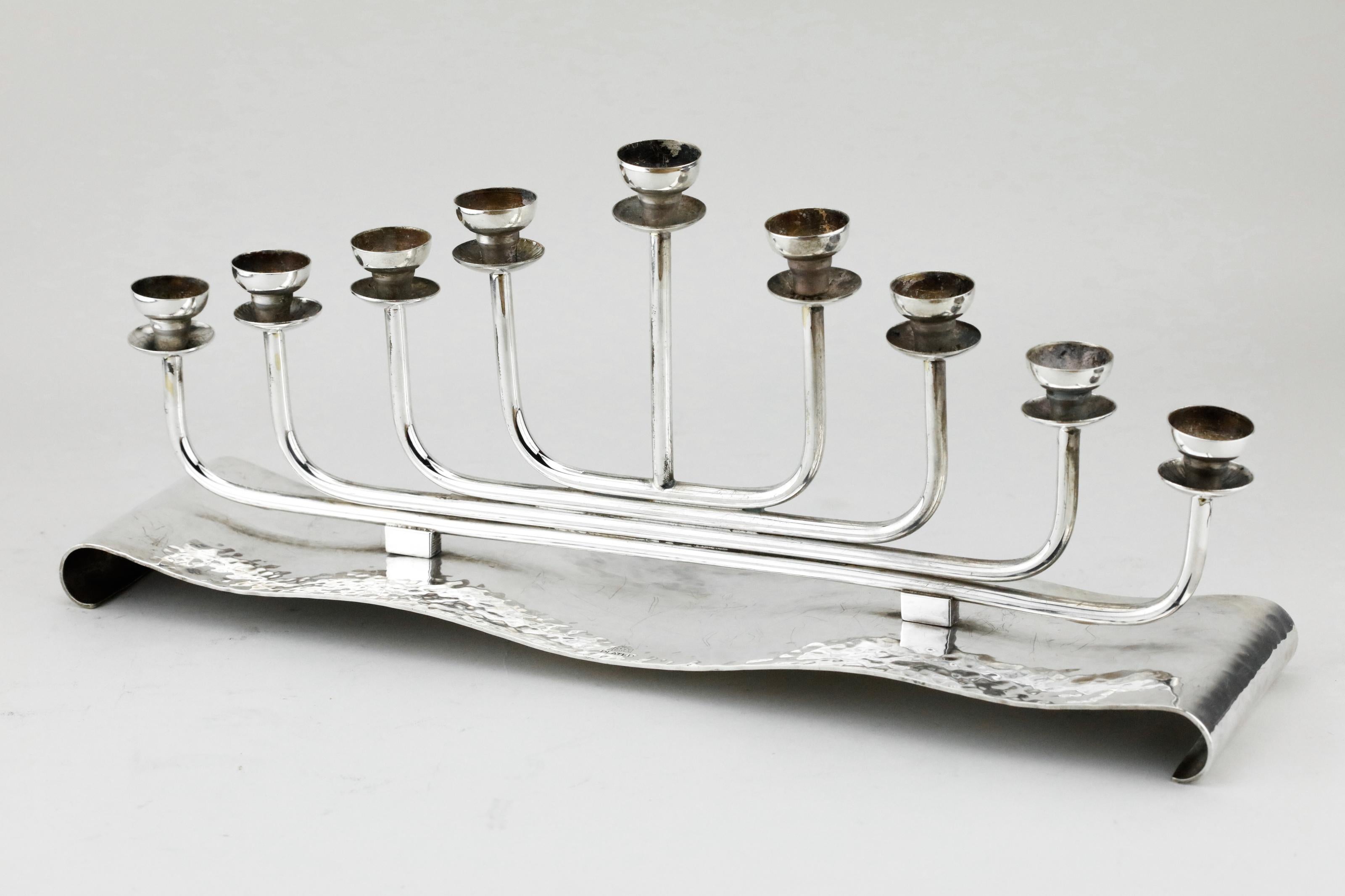 Handmade silver plated brass Hanukkah lamp Menorah, Austria, circa 1920.
In Bauhaus style. Hammered base with hand-forged branches, ends with candle holders with handcut wax guards.
Marked on the base: B.W. Austria.

Every item in Menorah Galleries