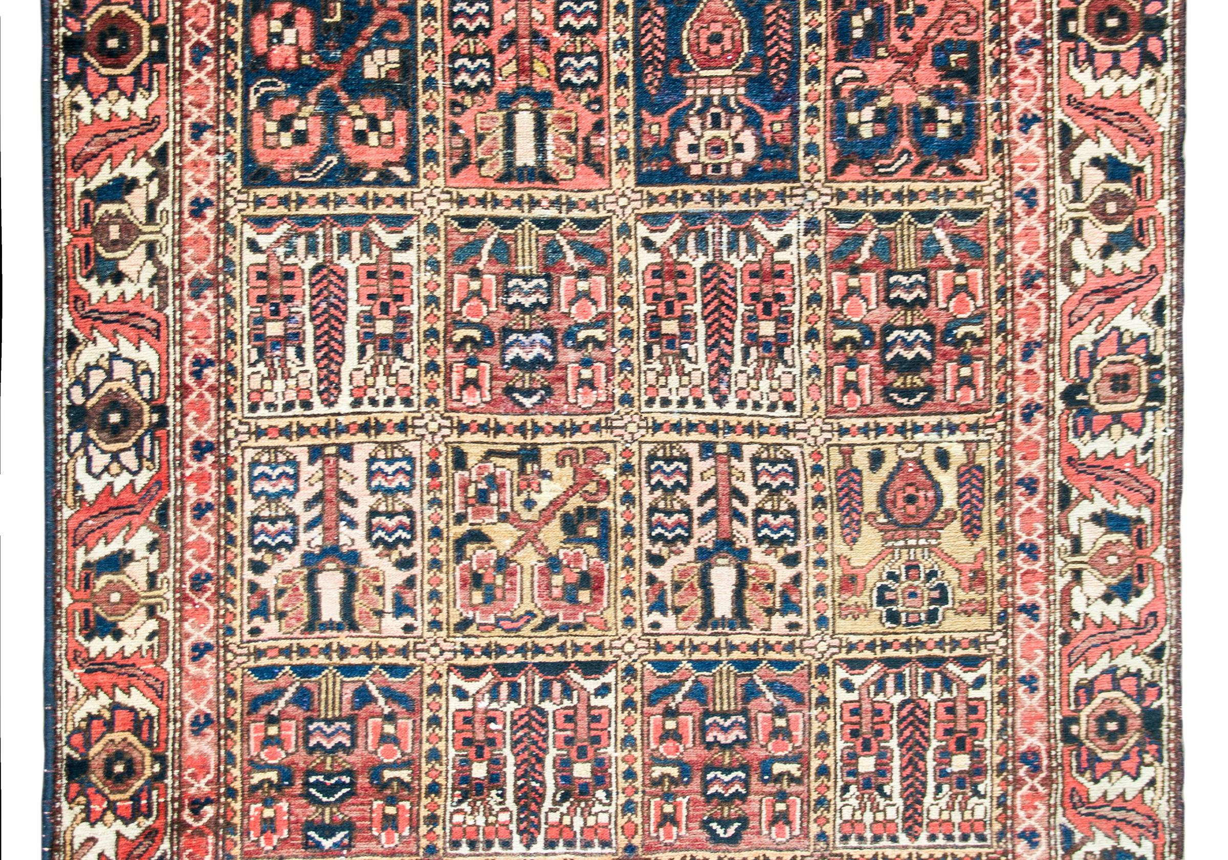 A wonderful early 20th century Persian Bakhtiari rug with a hand-woven patchwork pattern with myriad cypress trees and flowering shrubs surrounded by a wide scrolling vine and leaf border, and all woven in brilliant crimson, indigo, cream, green,