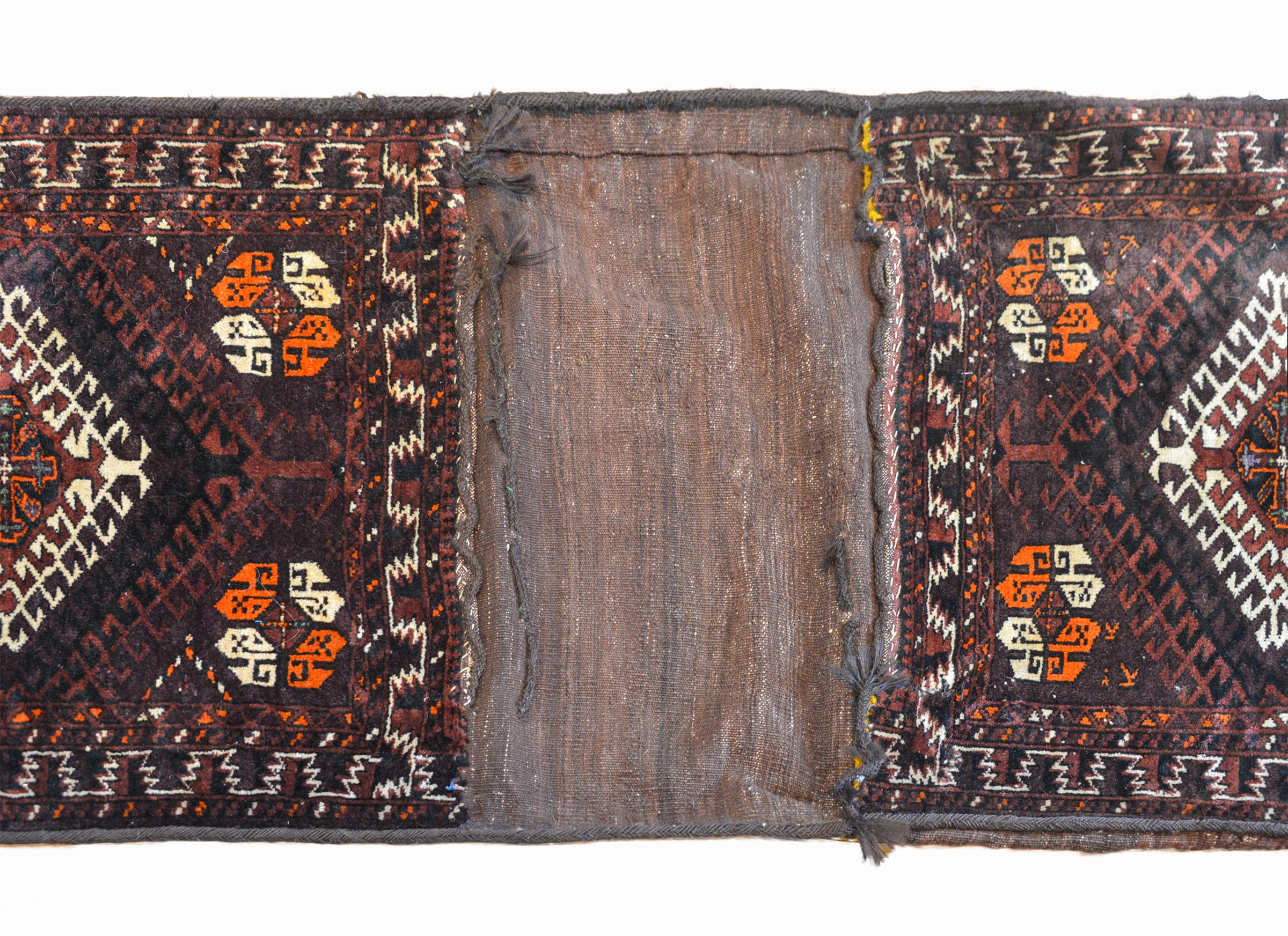 An early 20th century Persian Baluch saddle bag rug with each face having two white diamonds surrounded by two shades of brown, black, and copper colored wool. The borders are geometric woven in similarly colored wool.