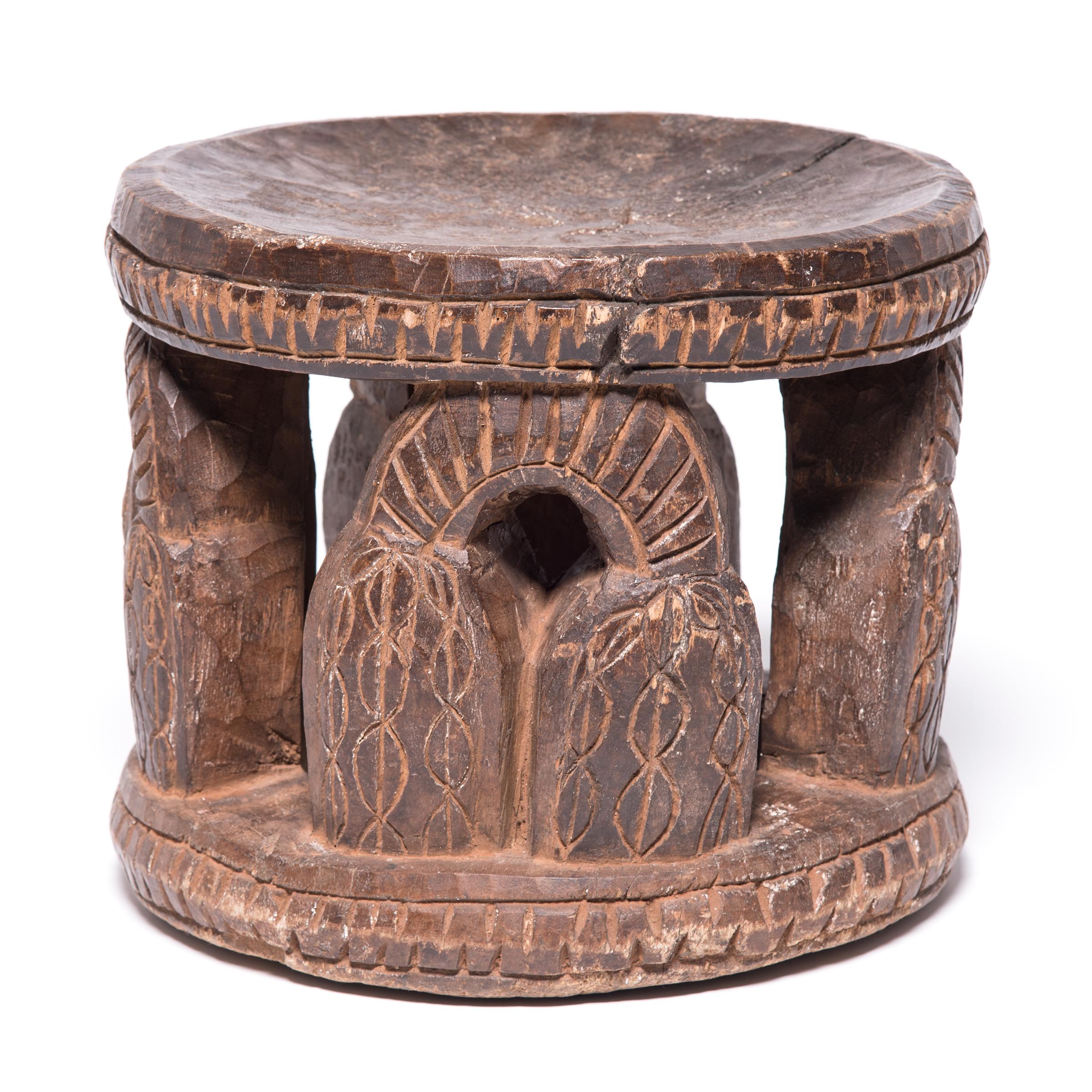 Marked by the telltale Bamileke rounded disc seat and base, this stool is supported with unexpected carvings of currency bells. Carved out of a single tree trunk, the bells both decorate and support the seated individual. The double bells were