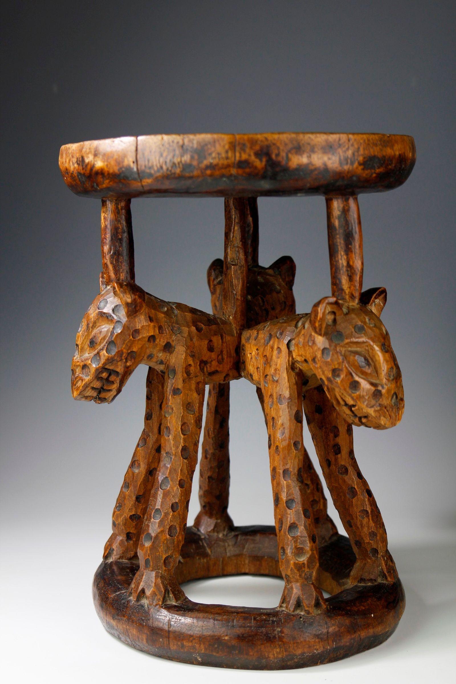 Carved from a single piece of wood, this stool from the Bamileke in the Cameroon, features at its centre three carved leopards with circular scorched decorations, representing their spots. The seat of the stool exhibits a lovely rippled surface, and