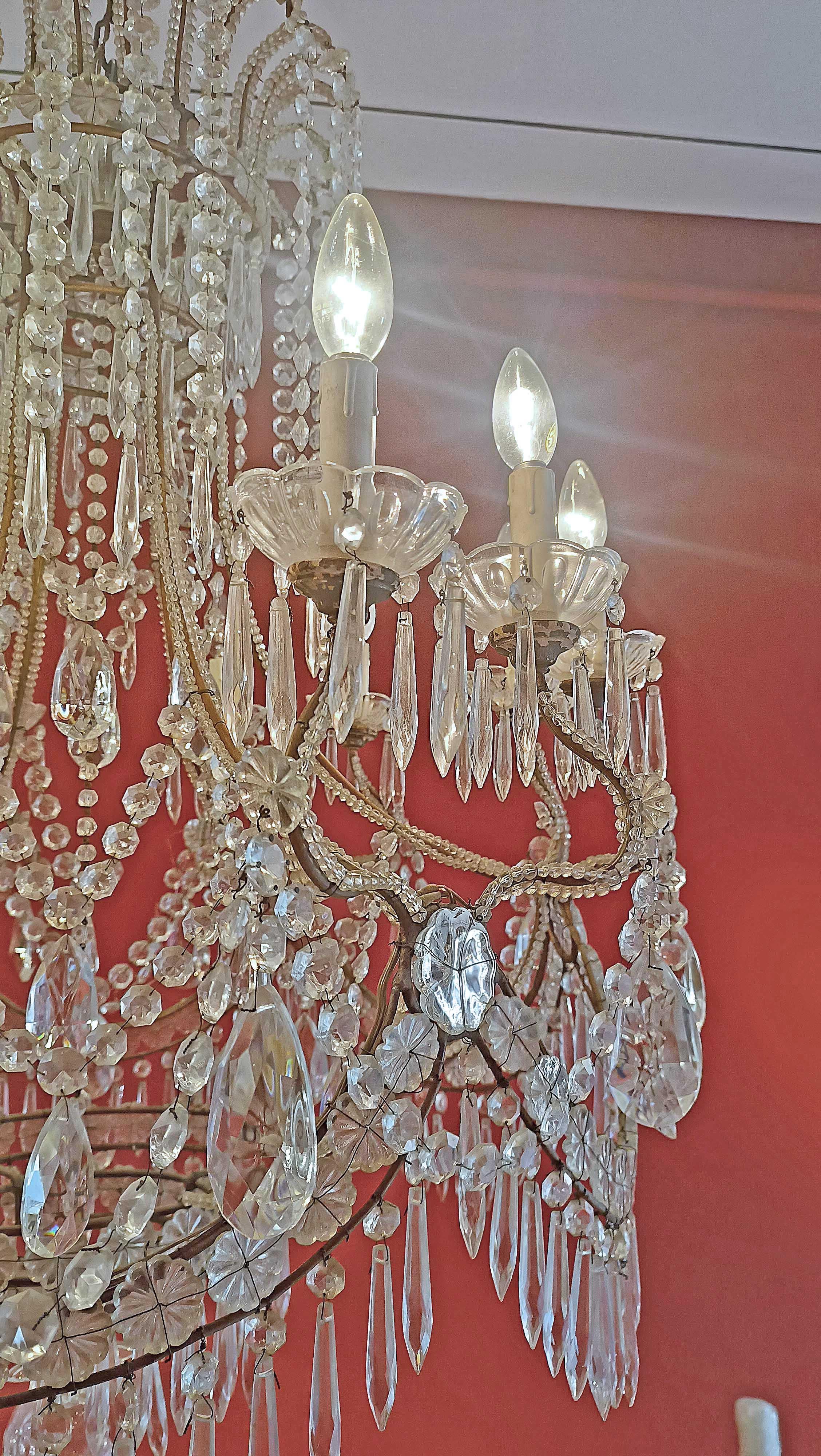 Elegant basket chandelier with a gilded metal structure, embellished with glass and crystal pendants. The chandelier has twelve lights and is electrified. Its soft and wavy shape, together with the presence of crystals, teardrop glass, pendants and