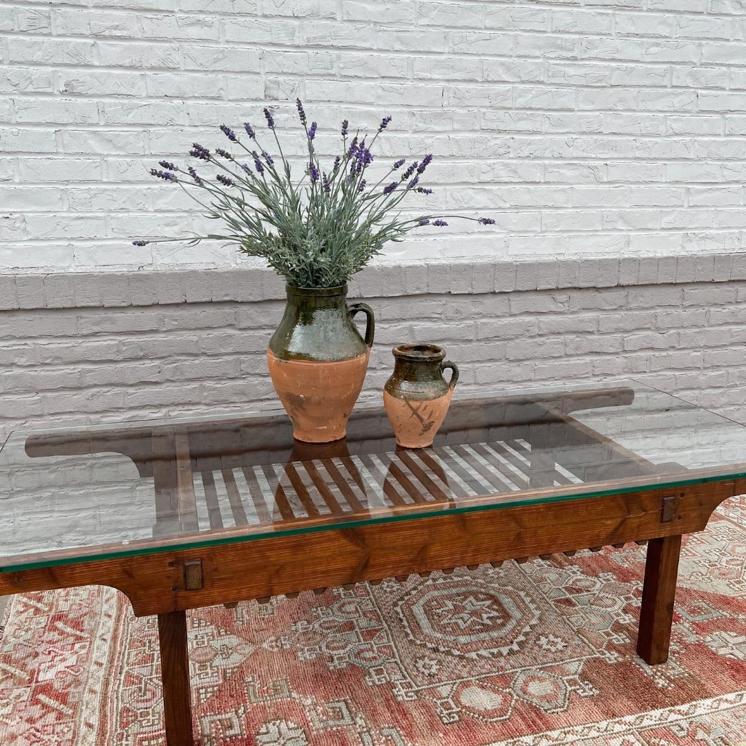 Circa 1920s Belgium. 

This antique coffee table is truly beautiful. Crafted out of warm wood and topped with a glass top, this table is sure to be a conversation starter. Wooden slats line the base of the table, allowing for a deep display area
