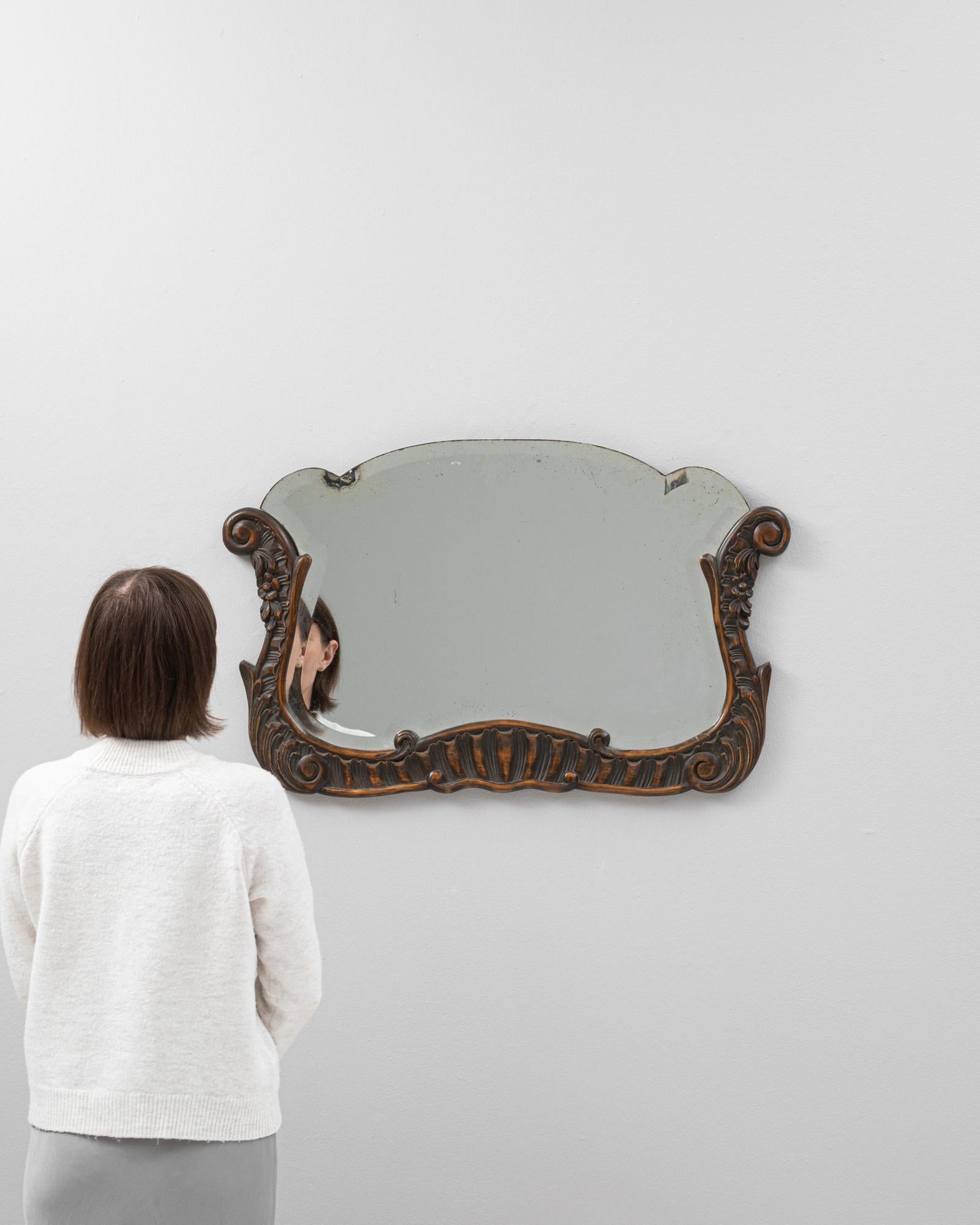 Ce miroir belge en bois du début du 20e siècle est une trouvaille exquise, imprégnée de l'élégance d'une époque révolue. Son cadre en bois orné, sculpté de détails et de fioritures complexes, porte la riche patine du temps, offrant un aspect